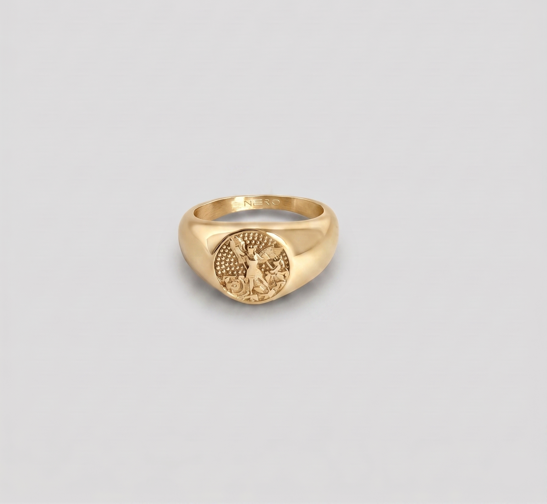 טבעת חותם (Signet ring) גברית בגוון זהב מבריק, עשויה פלדת אל-חלד. על החותם המעוגל חרוטה דמות שומר מפורטת בסגנון קלאסי על רקע טקסטורת נקודות. על הדופן הפנימית של הטבעת חרוט המותג "NERO".