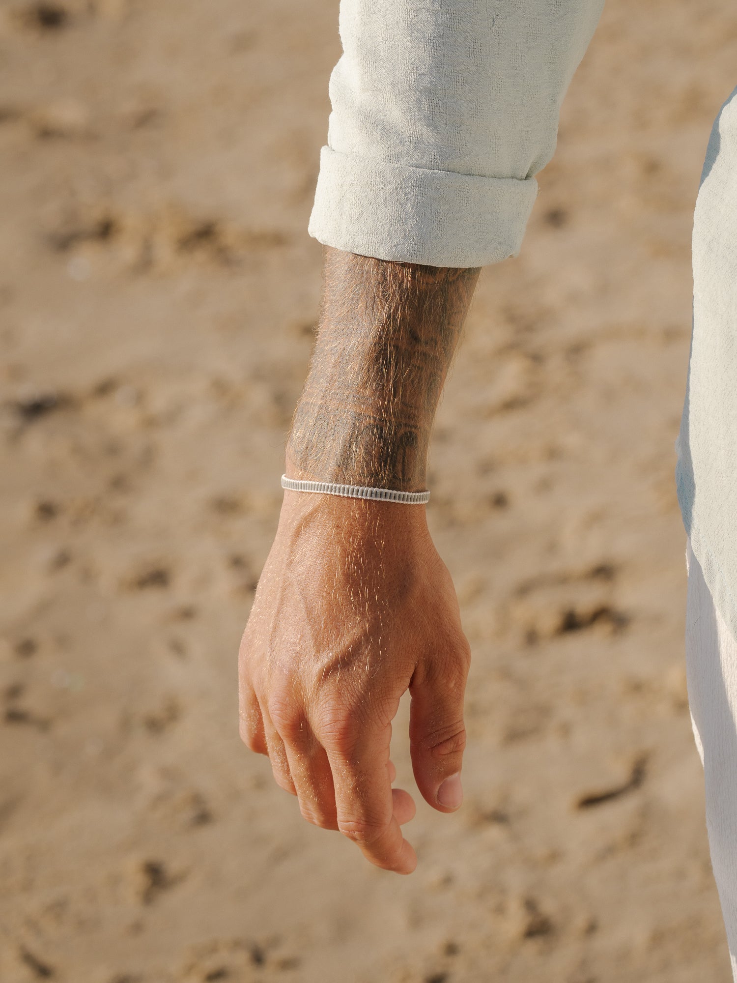 צמיד Aqua לבן או אפור בהיר על פרק כף יד של גבר, על רקע חול, שרוול לבן מופשל.