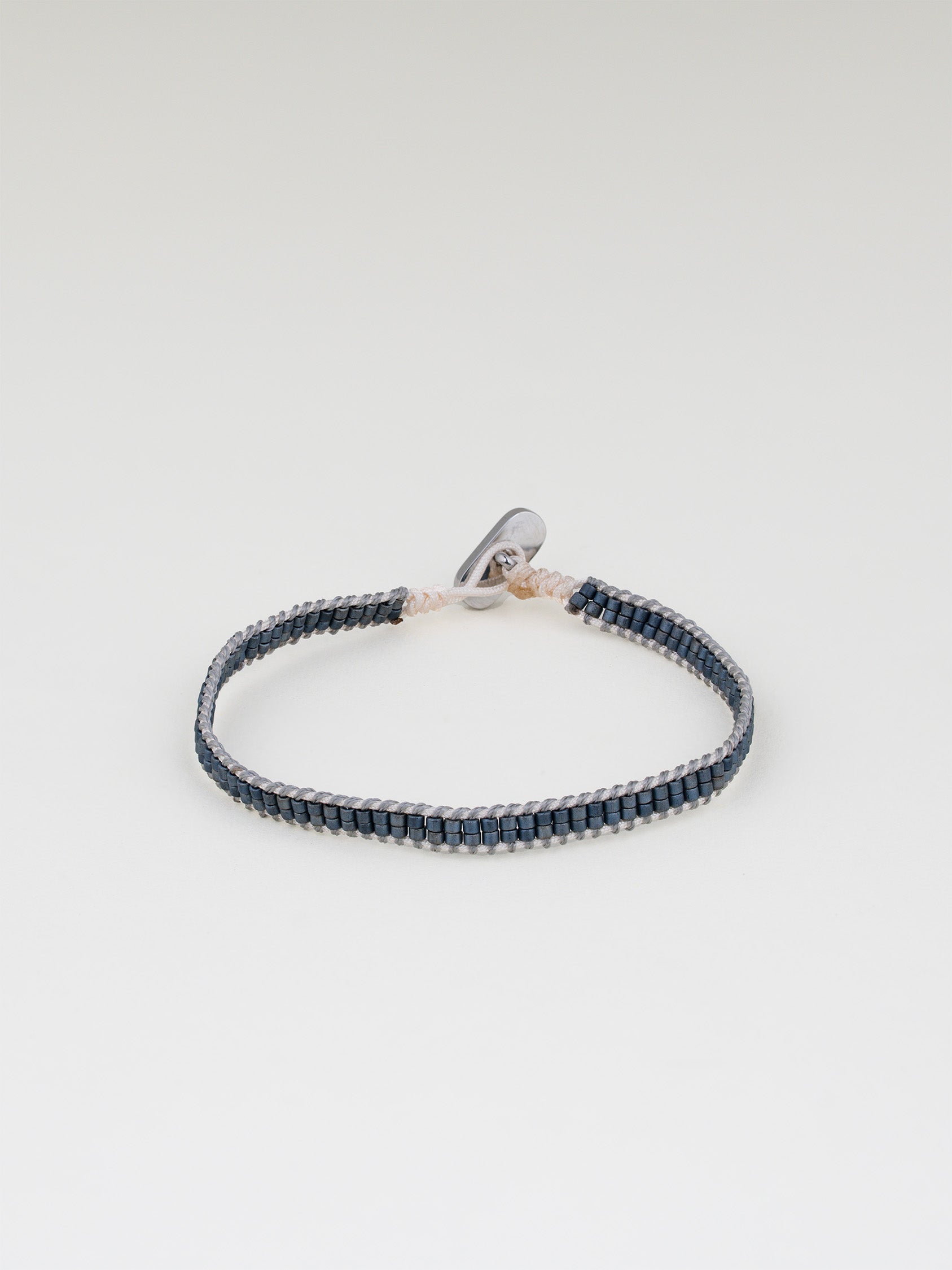 צמיד Aqua כחול כהה (נייבי) עדין, סרוג מחוט בהיר וחרוזים כחולים קטנים, על רקע לבן.