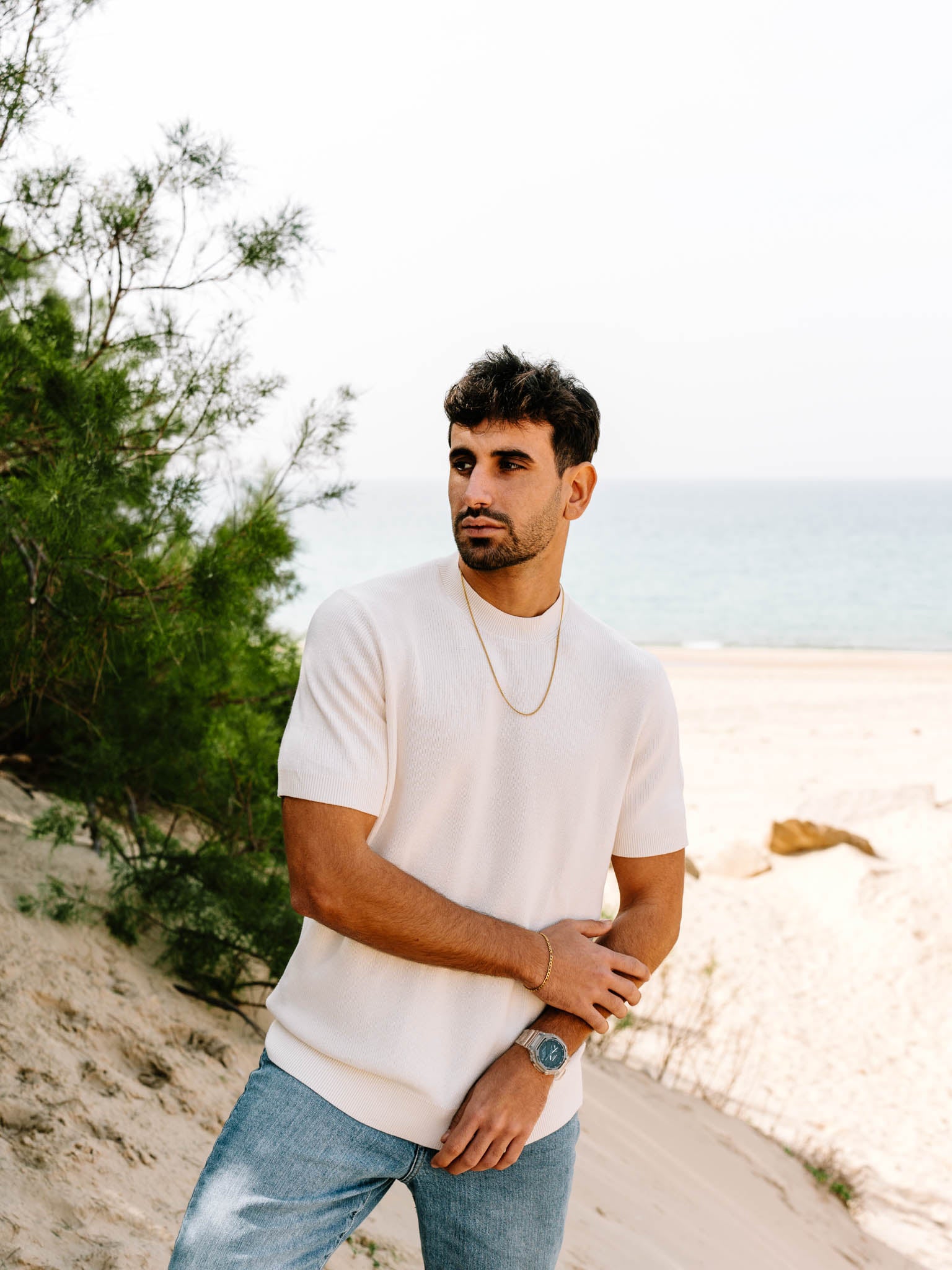 דוגמן עם סט תכשיטי Aura זהב – צמיד ושרשרת – מצולם על רקע חוף