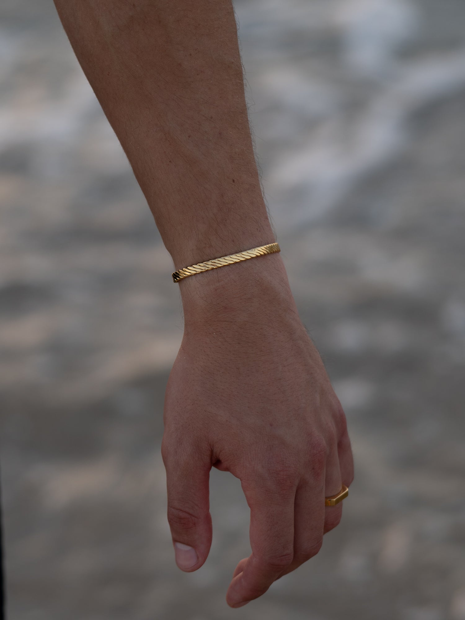 צמיד Beluga זהב בגימור מבריק על פרק כף היד של גבר, בצילום תקריב בחוף.