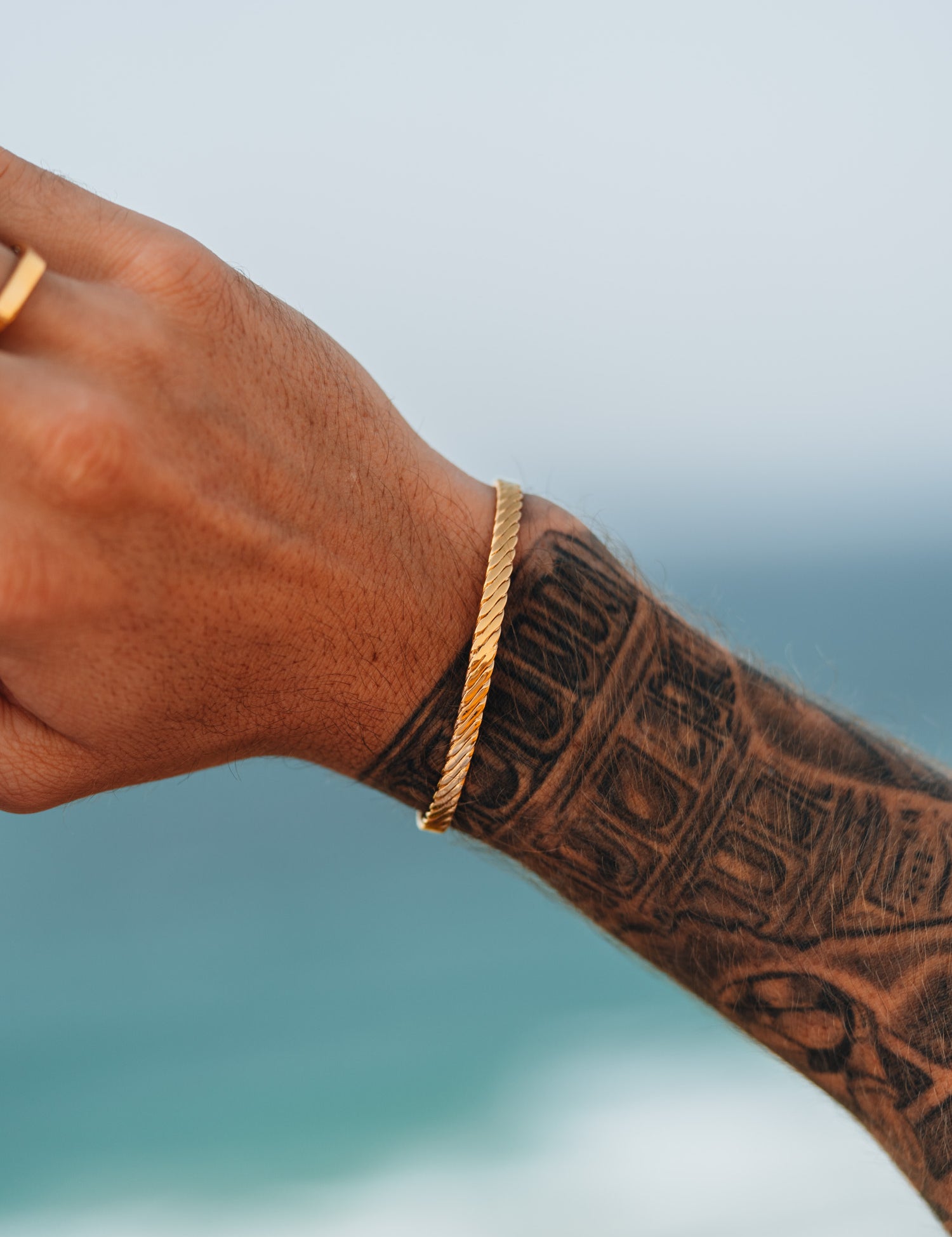 צמיד Beluga זהב על יד מקועקעת, על רקע הים והשמיים.