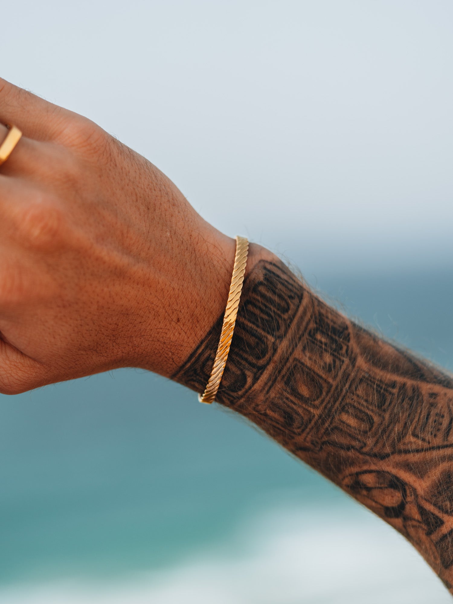 צמיד Beluga זהב על יד מקועקעת, על רקע הים והשמיים.