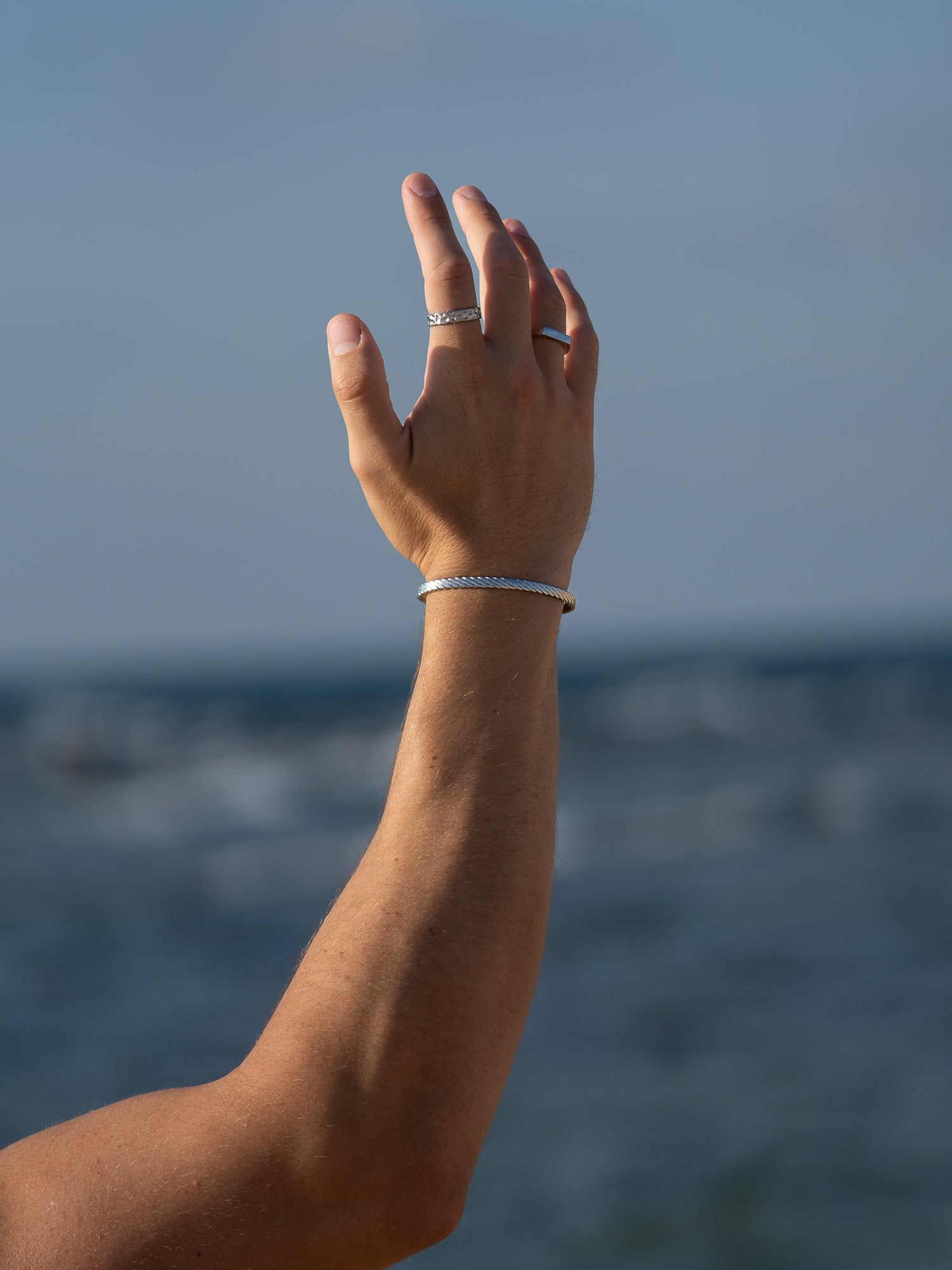 צמיד Beluga כסף על פרק יד גברית, משולב עם טבעות Meduza נוספות, על רקע ים כחול.