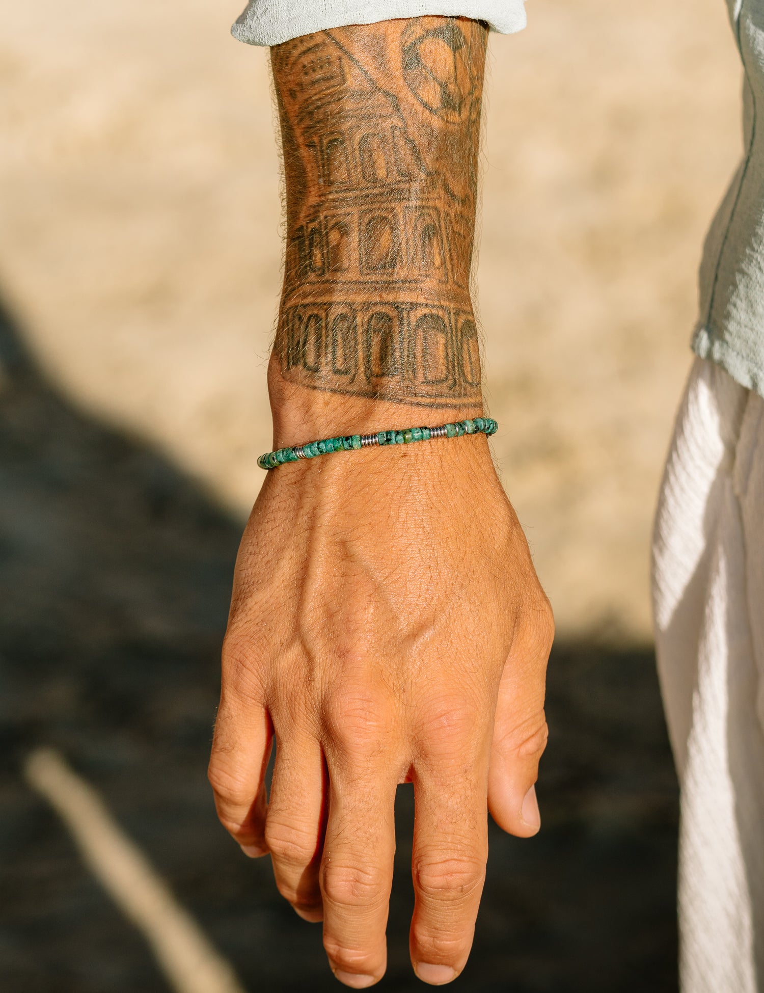 צמיד Bloom טורקיז לגבר על פרק היד, בסטיילינג חוף עם חולצה פתוחה.