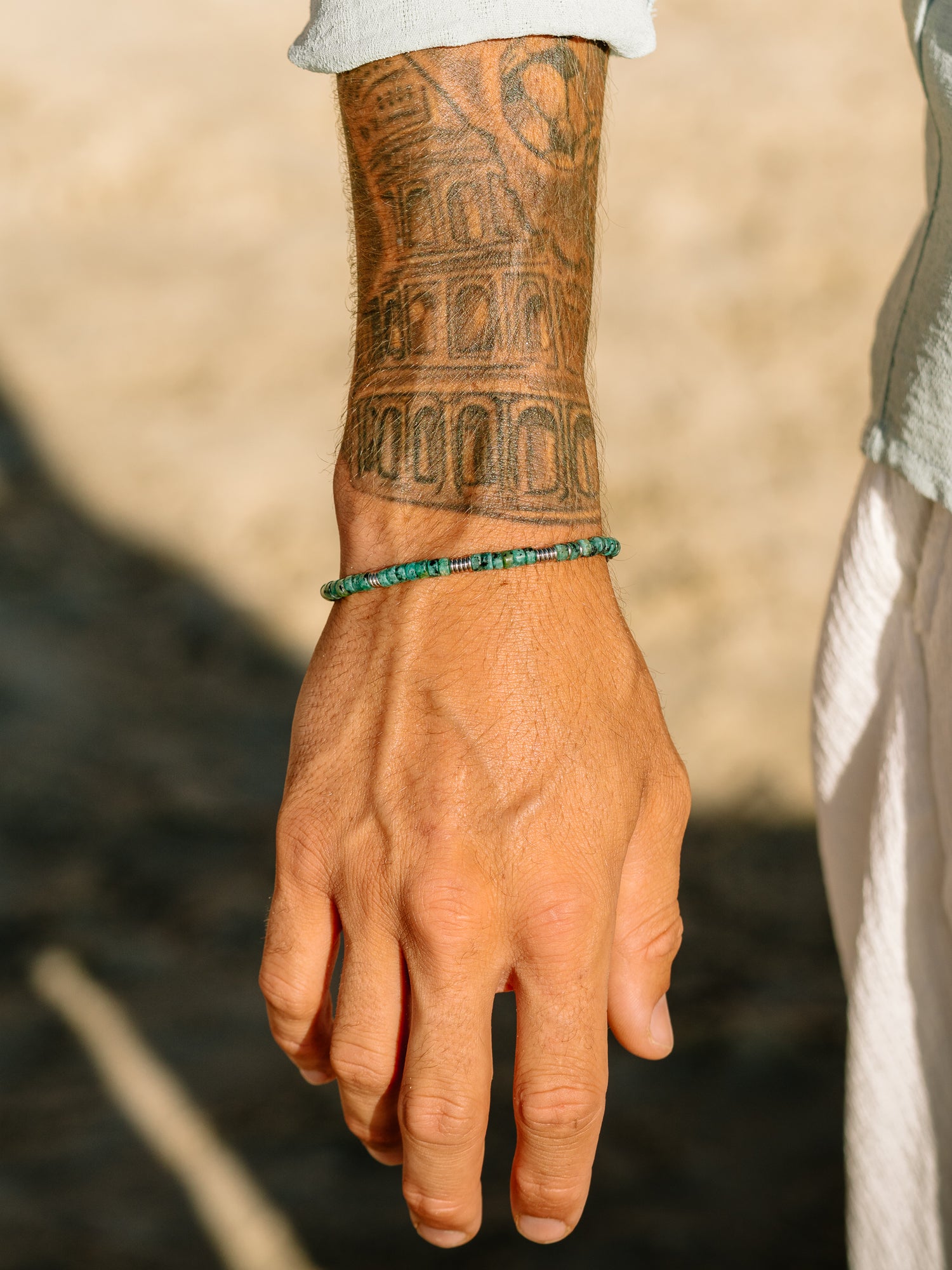 צמיד Bloom טורקיז לגבר על פרק היד, בסטיילינג חוף עם חולצה פתוחה.