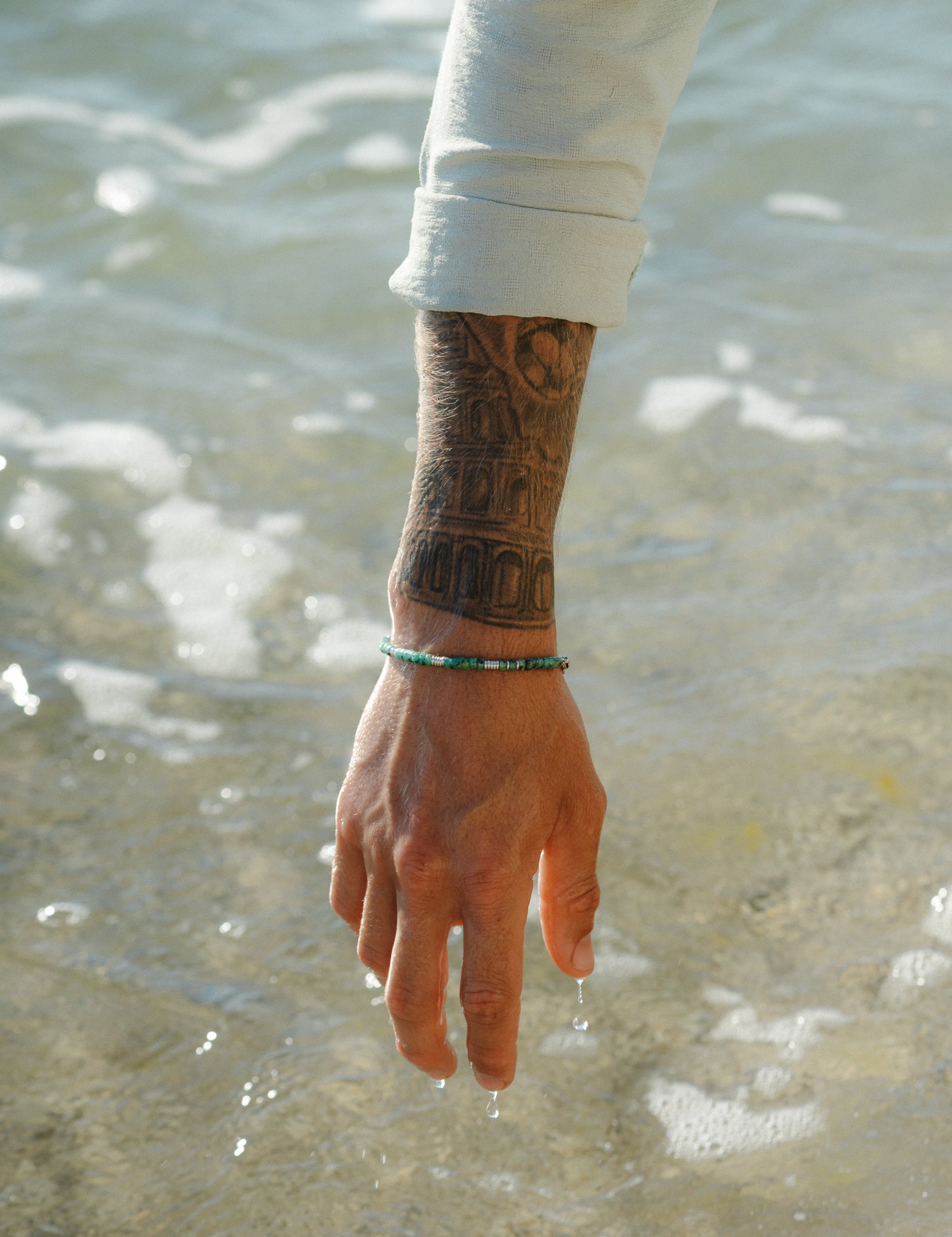 צמיד Bloom טורקיז בסטיילינג ימי עם צמיד וכף וכסף, נוגע במים רדודים.