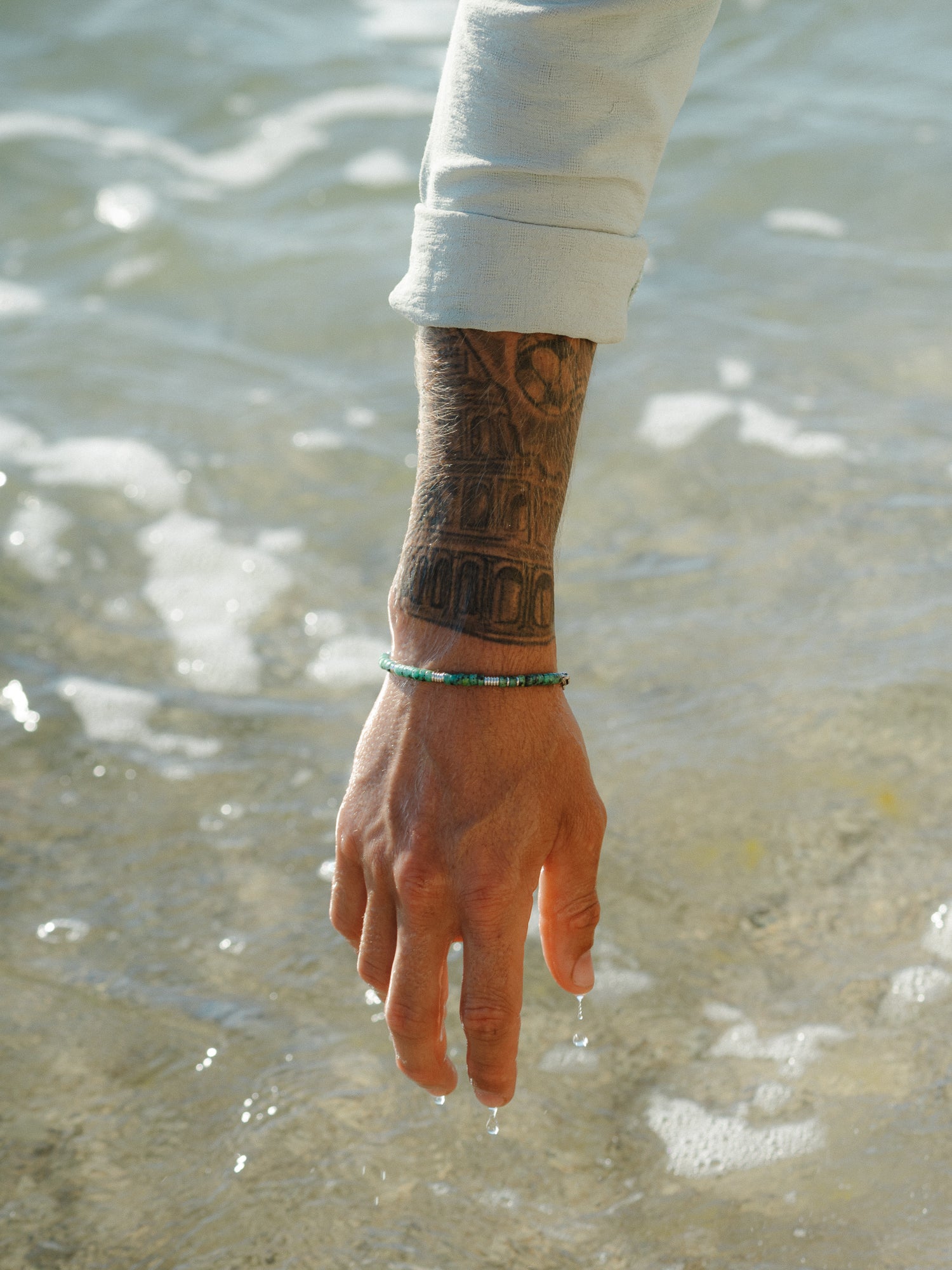 צמיד Bloom טורקיז בסטיילינג ימי עם צמיד וכף וכסף, נוגע במים רדודים.