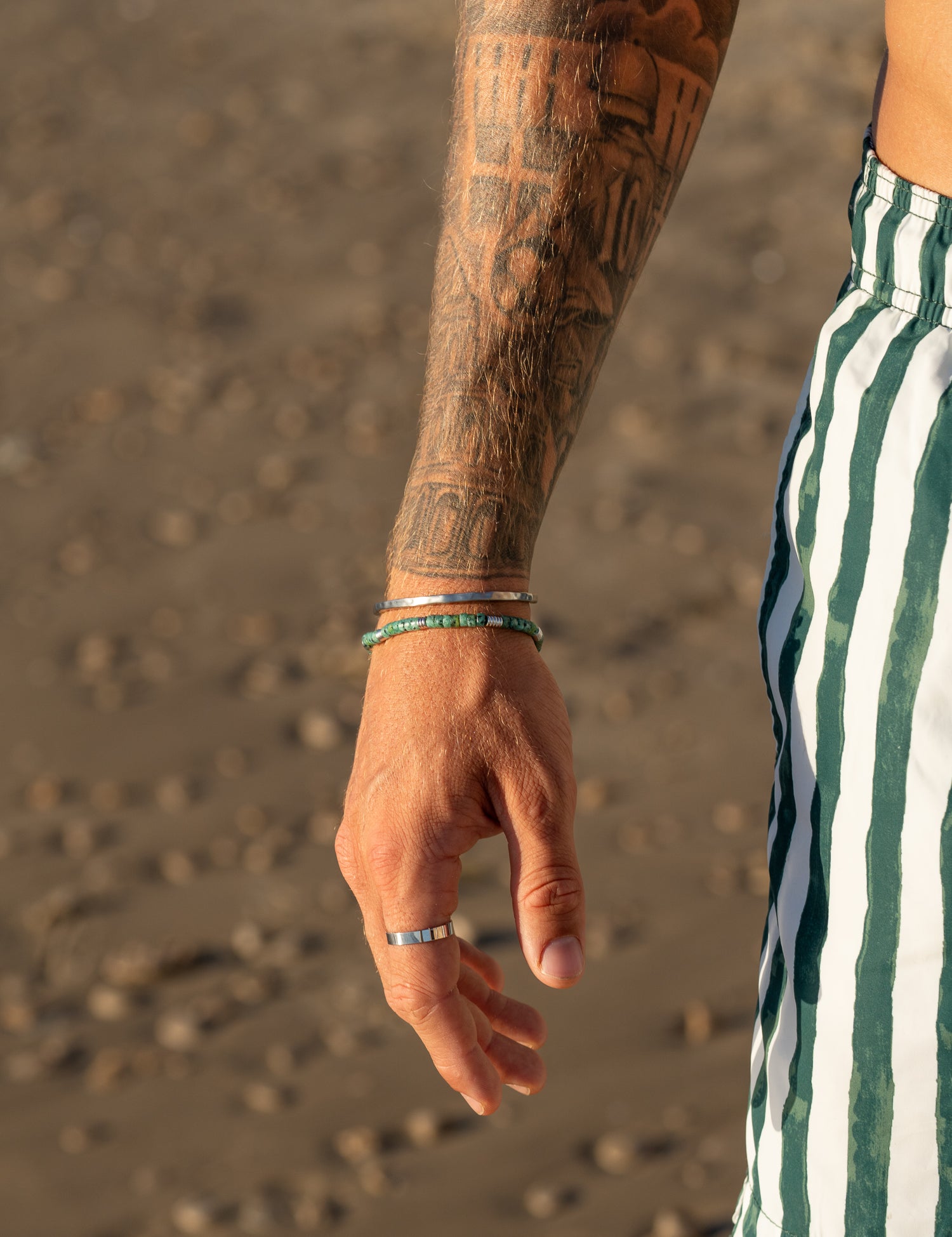 צמיד Bloom טורקיז לגבר משולב עם טבעות וכסף, צילום סטיילינג על חול רטוב בחוף.