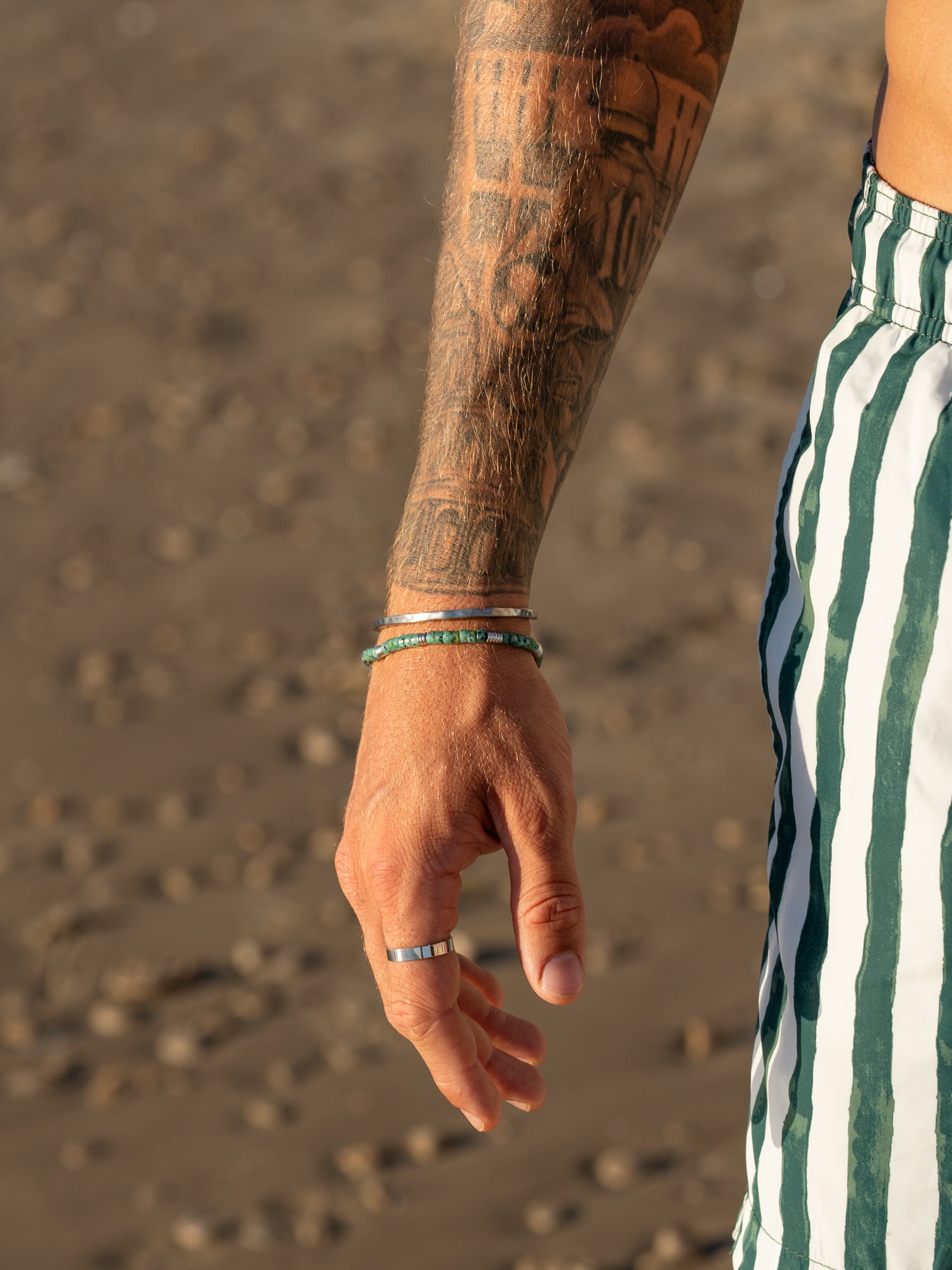 צמיד Bloom טורקיז לגבר משולב עם טבעות וכסף, צילום סטיילינג על חול רטוב בחוף.