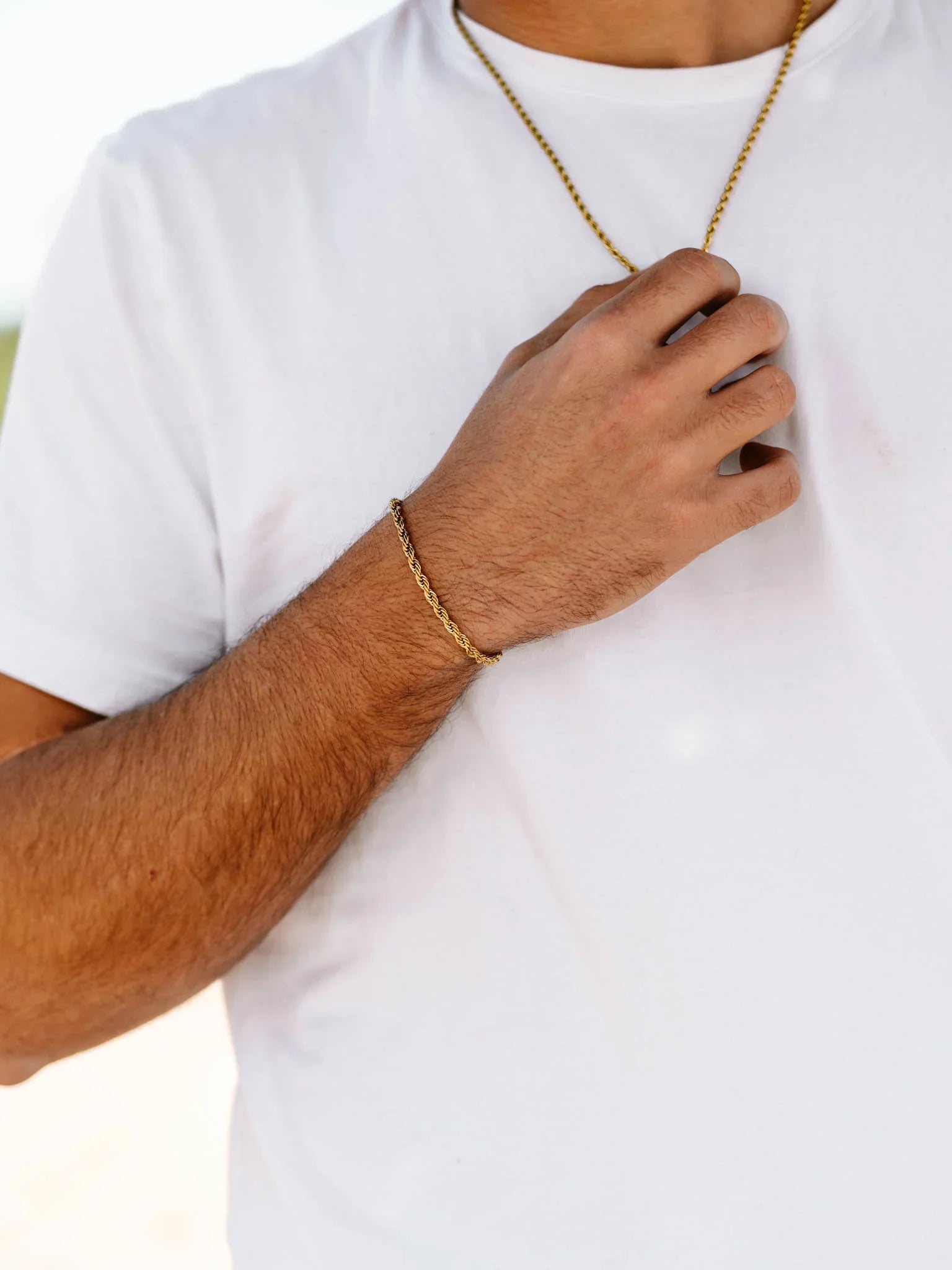 גבר לובש צמיד Eros זהב ושרשרת תואמת של NERO על רקע חולצה לבנה