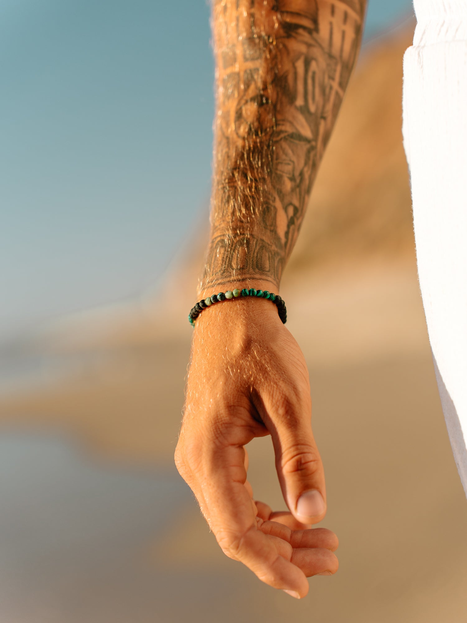 צמיד Kai לגבר (מלכיט ולבה) על פרק יד גברי, משולב עם טבעות כסף, על רקע כחול של האוקיינוס.