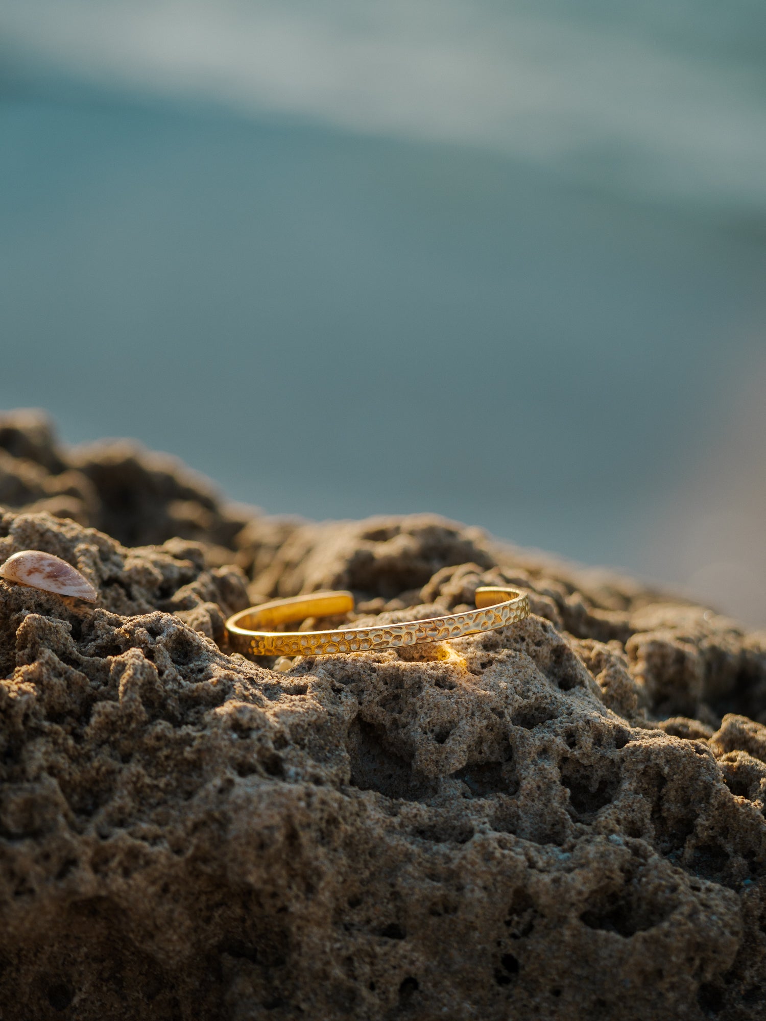 צמיד Meduza בזהב מונח על סלע חוף ים, בסטייל נקי ואלגנטי.