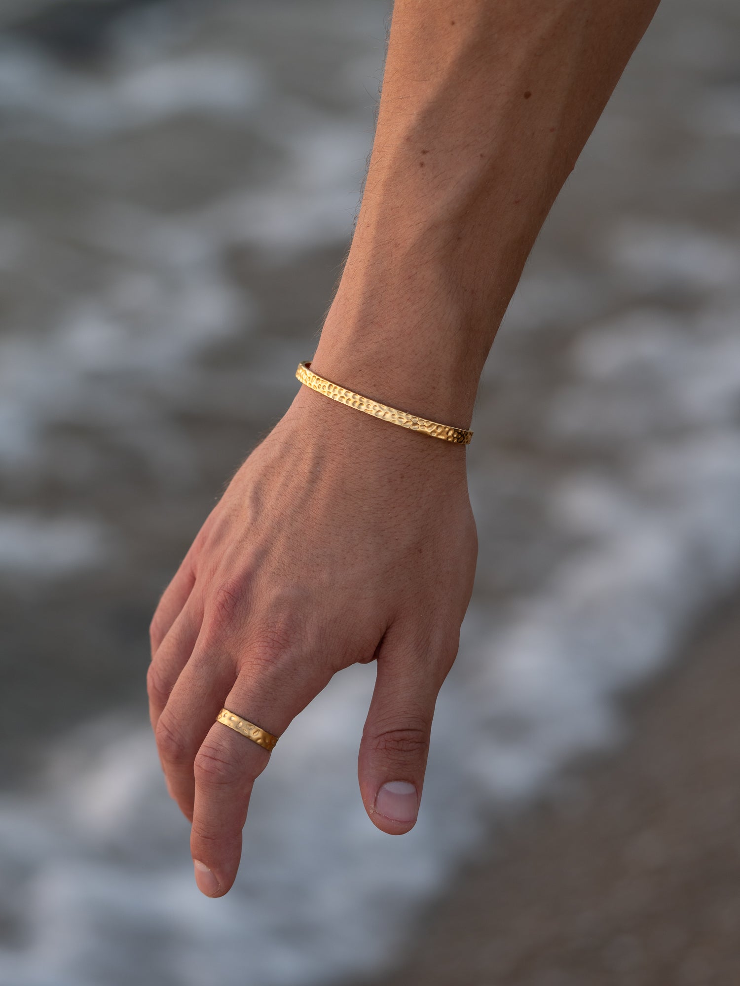 תקריב על צמיד וטבעת Meduza לגבר בזהב, עם טקסטורה ייחודית על רקע קצף גלי הים.