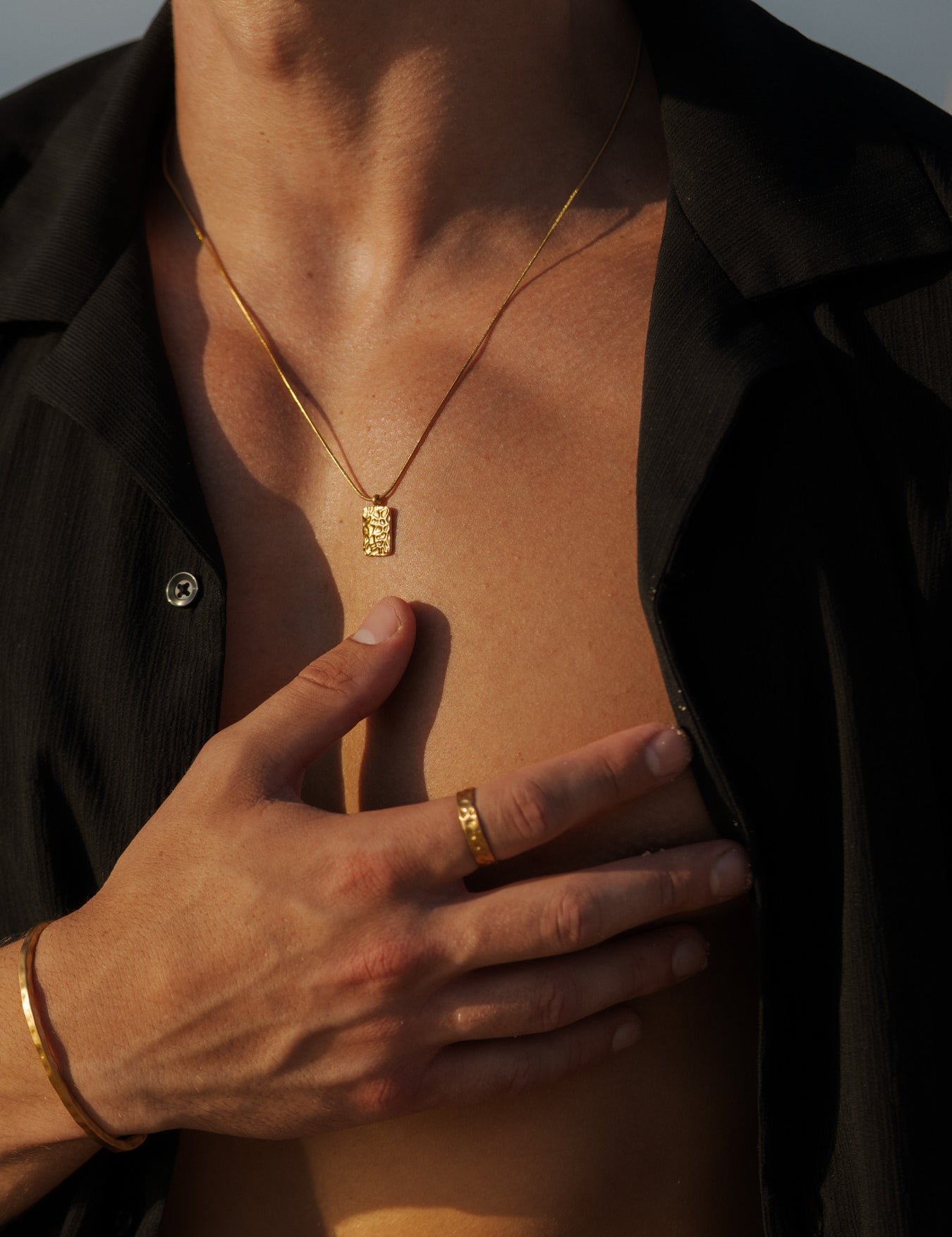 שרשרת Meduza זהב ותליון מבריק, מעוצבת על דגם עם חולצה שחורה.