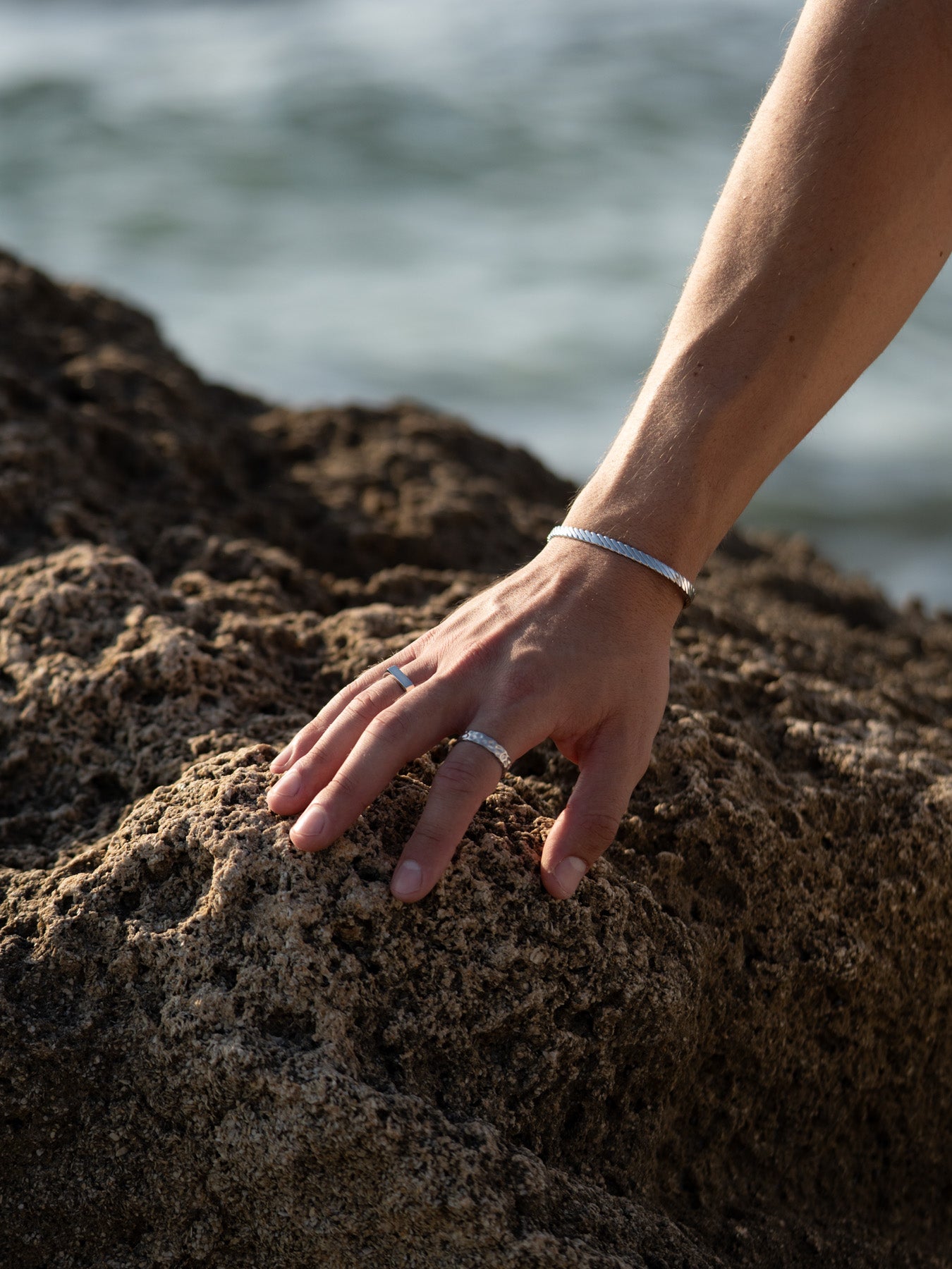 טבעת Meduza לגבר בזהב, בגימור מט, מוחזקת על ידי גבר מול רקע מים.