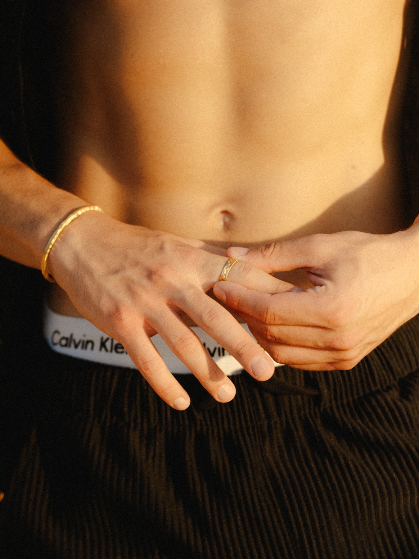 טבעת Meduza זהב לגבר בגימור מט, על רקע כף יד גברית עונדת צמיד רחב.