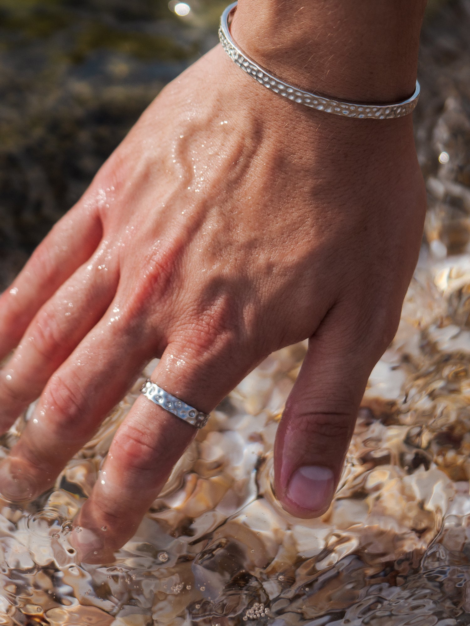 טבעת Meduza כסף בגימור מט על אצבע גברית, על רקע חוף רטוב ומים.