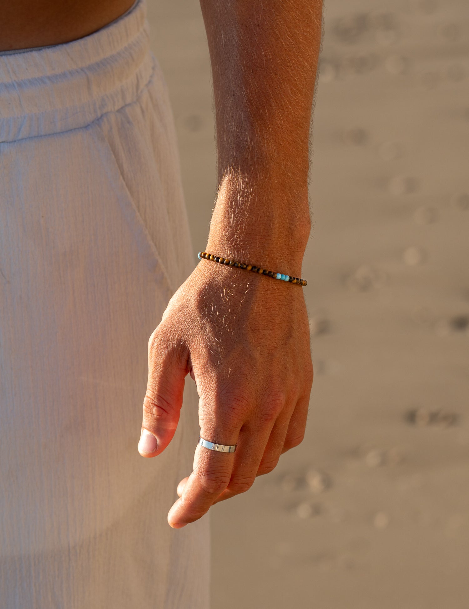 צמיד Mistral יוקרתי (עין הנמר וטורקיז) על פרק יד גברי, צילום תקריב בחוף הים.