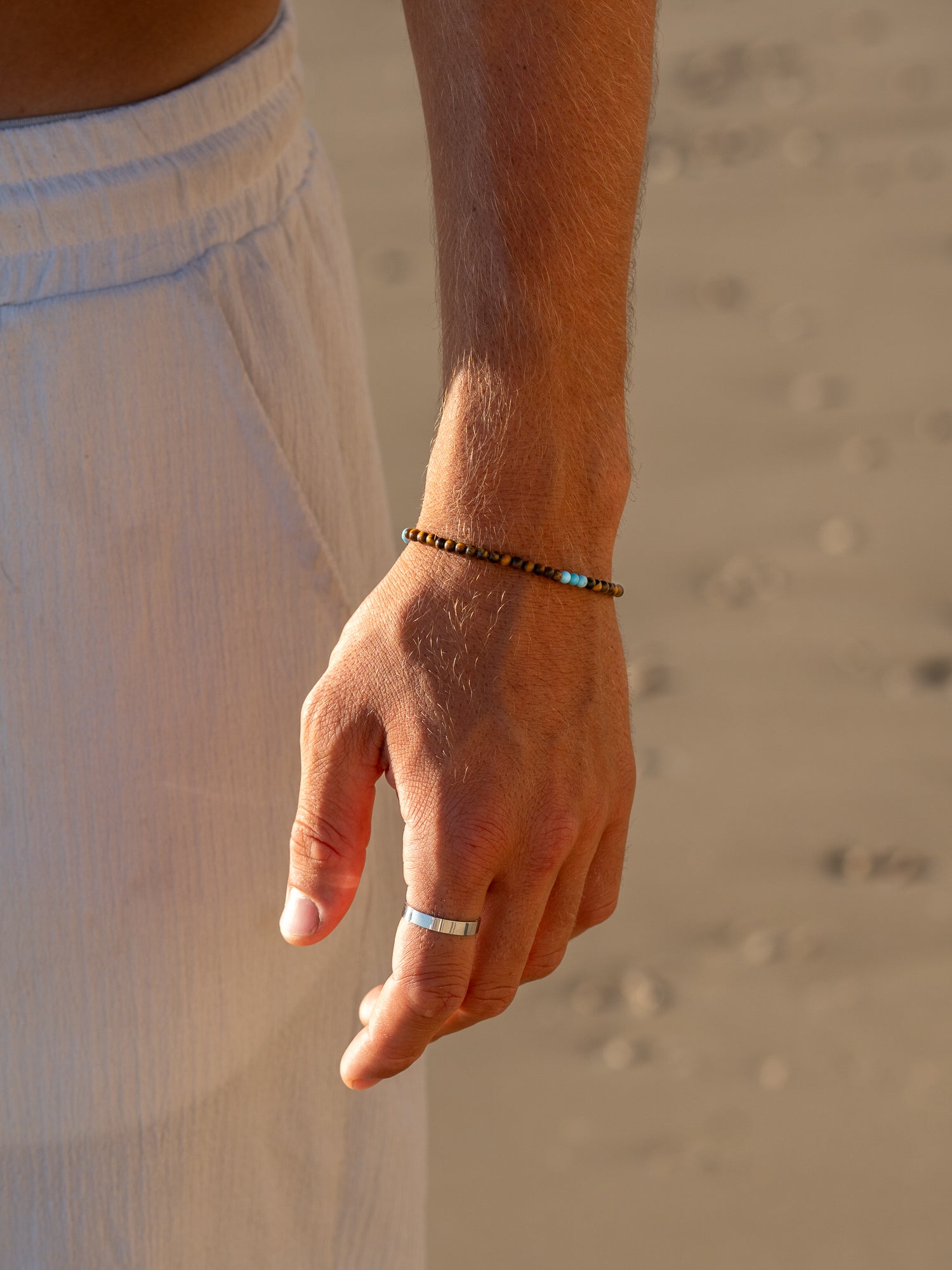 צמיד Mistral יוקרתי (עין הנמר וטורקיז) על פרק יד גברי, צילום תקריב בחוף הים.