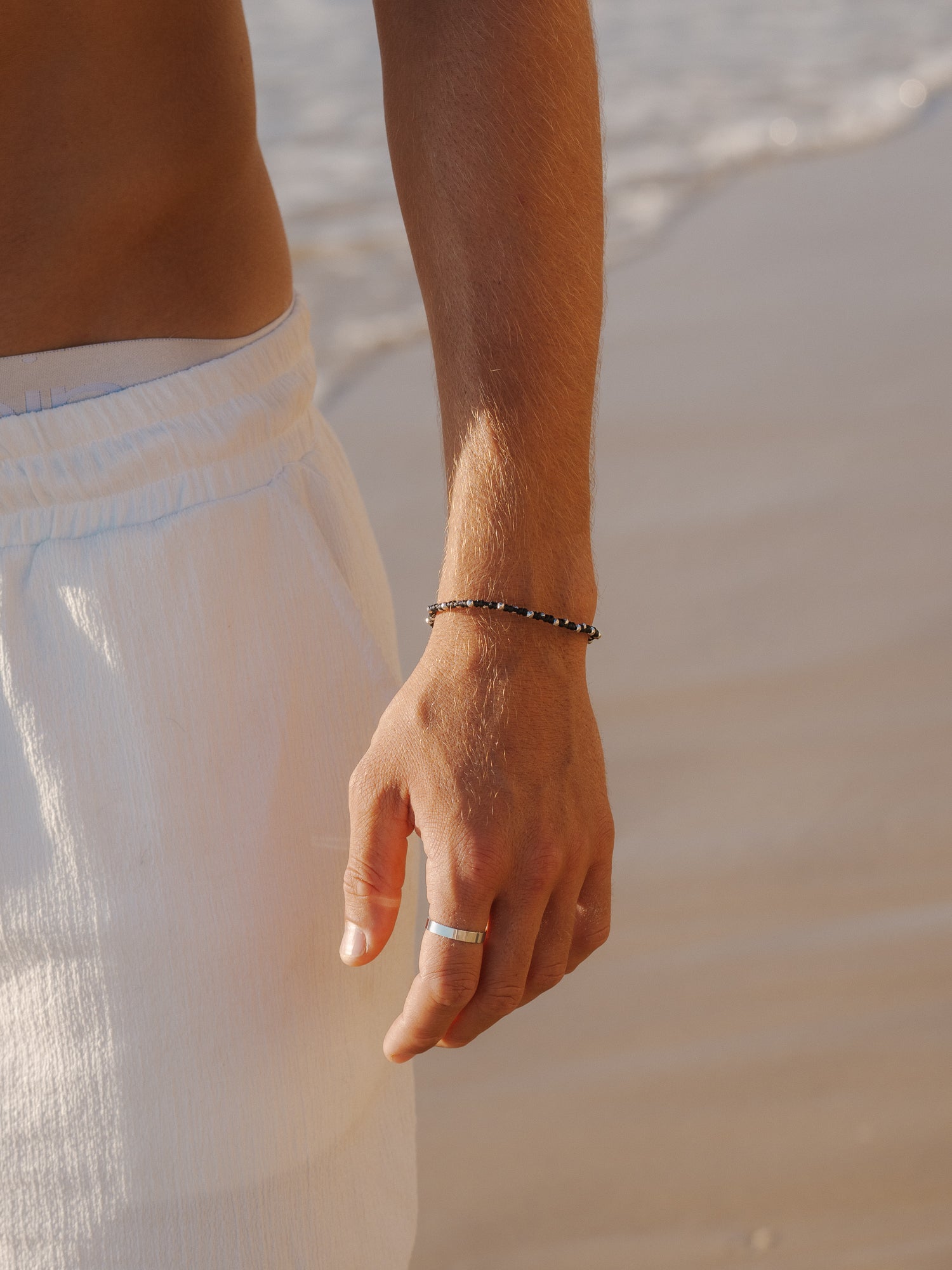 צמיד Moonstone (חוט שעווה) משולב עם צמיד Reef כסף מט (דק), בצילום ימי על רקע מים.