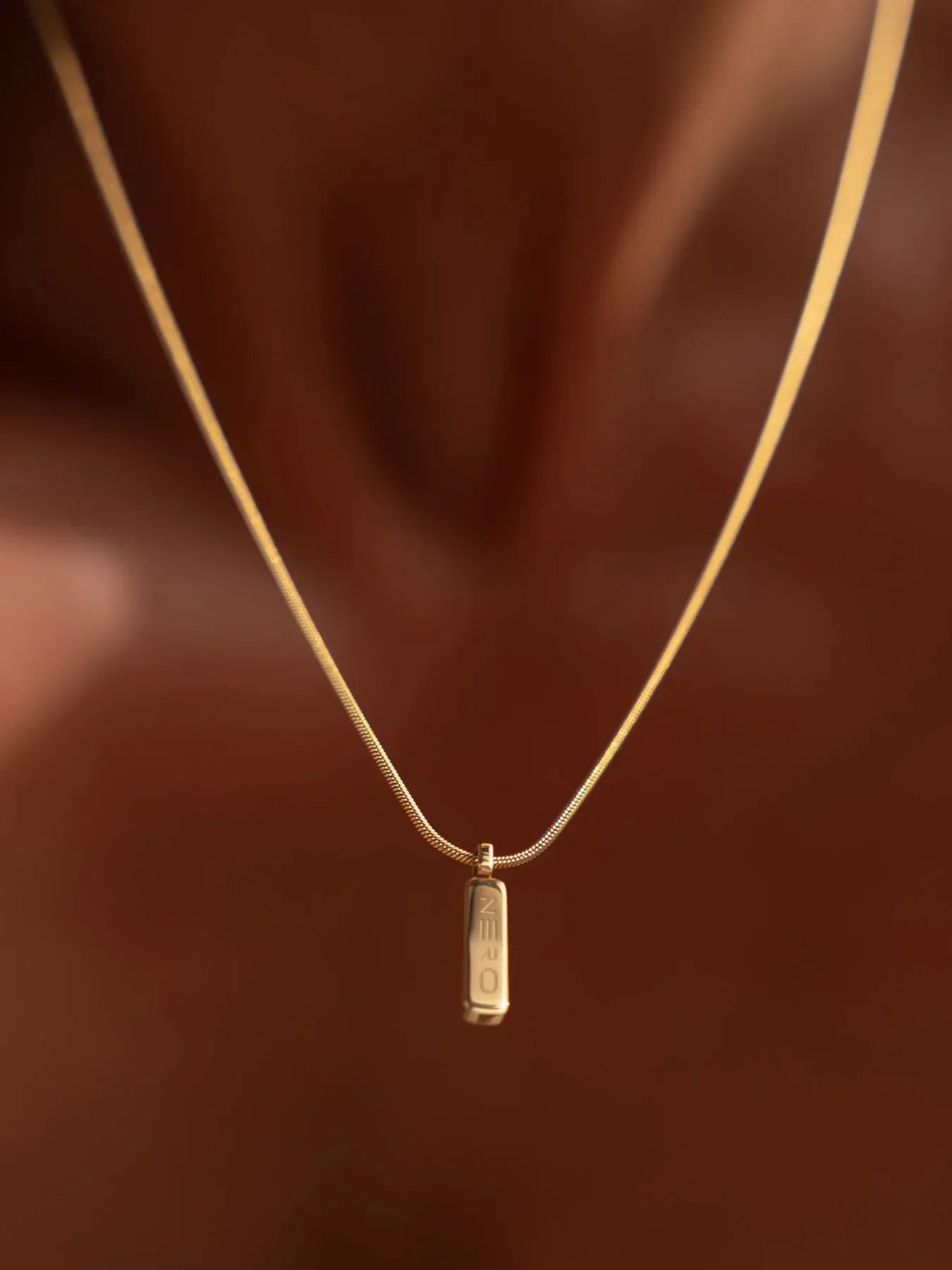 שרשרת Manta מזהב על צוואר, תליון מלבני עם לוגו NERO, צילום תקריב על רקע עור בגוון חם.
