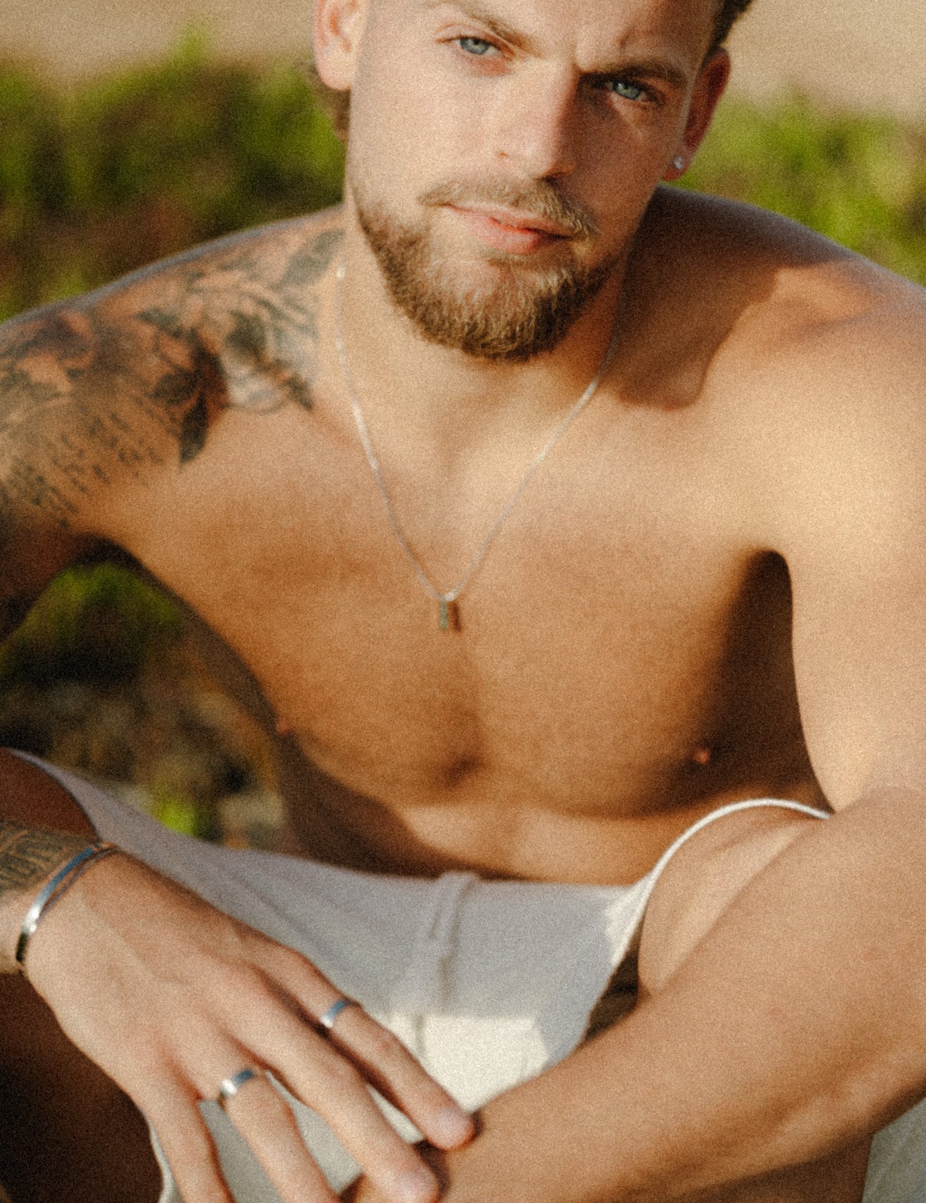 דוגמן יושב על החוף עונד שרשרת Manta של NERO בגימור כסף, בצילום טבעי באור שמש