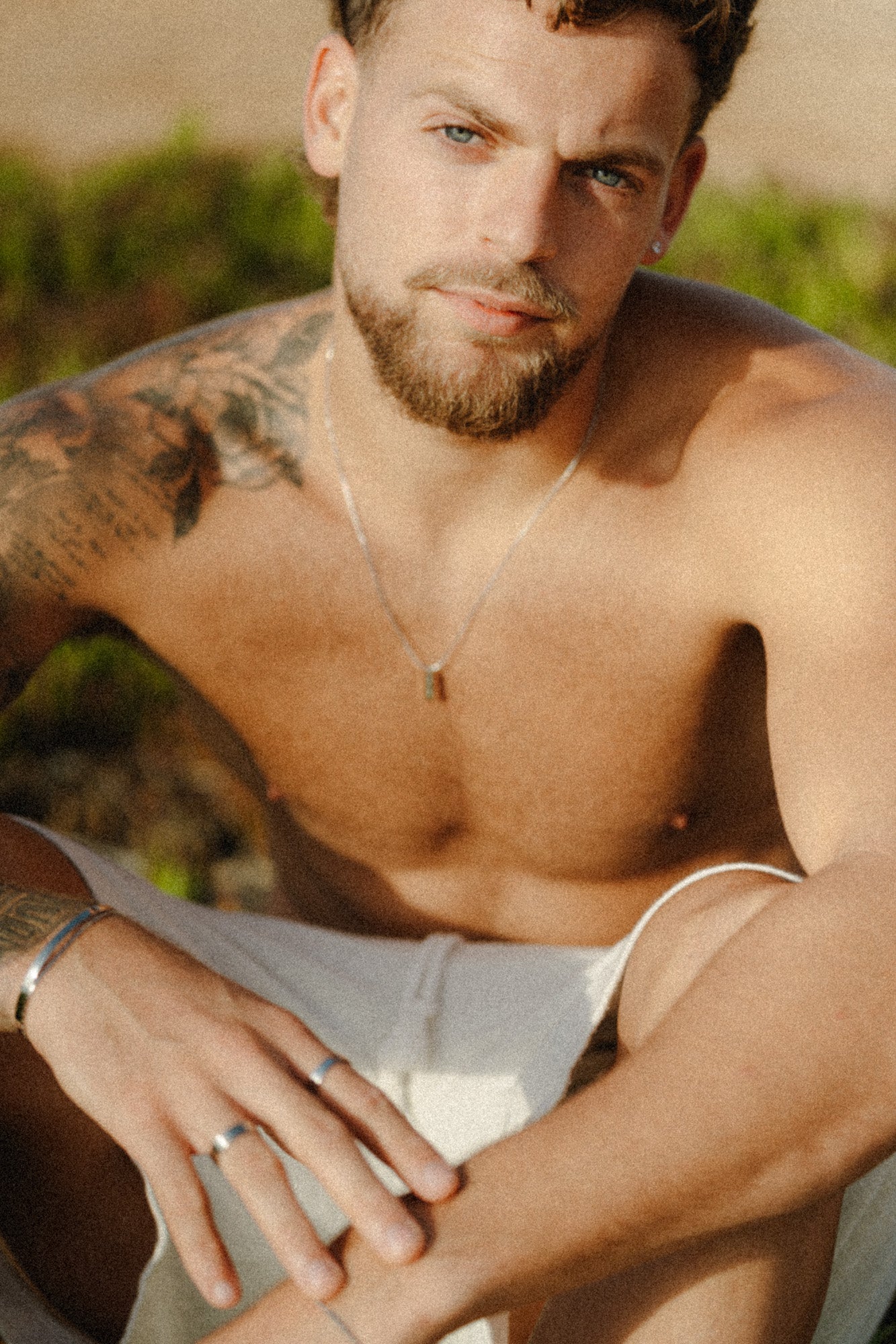 דוגמן יושב על החוף עונד שרשרת Manta של NERO בגימור כסף, בצילום טבעי באור שמש