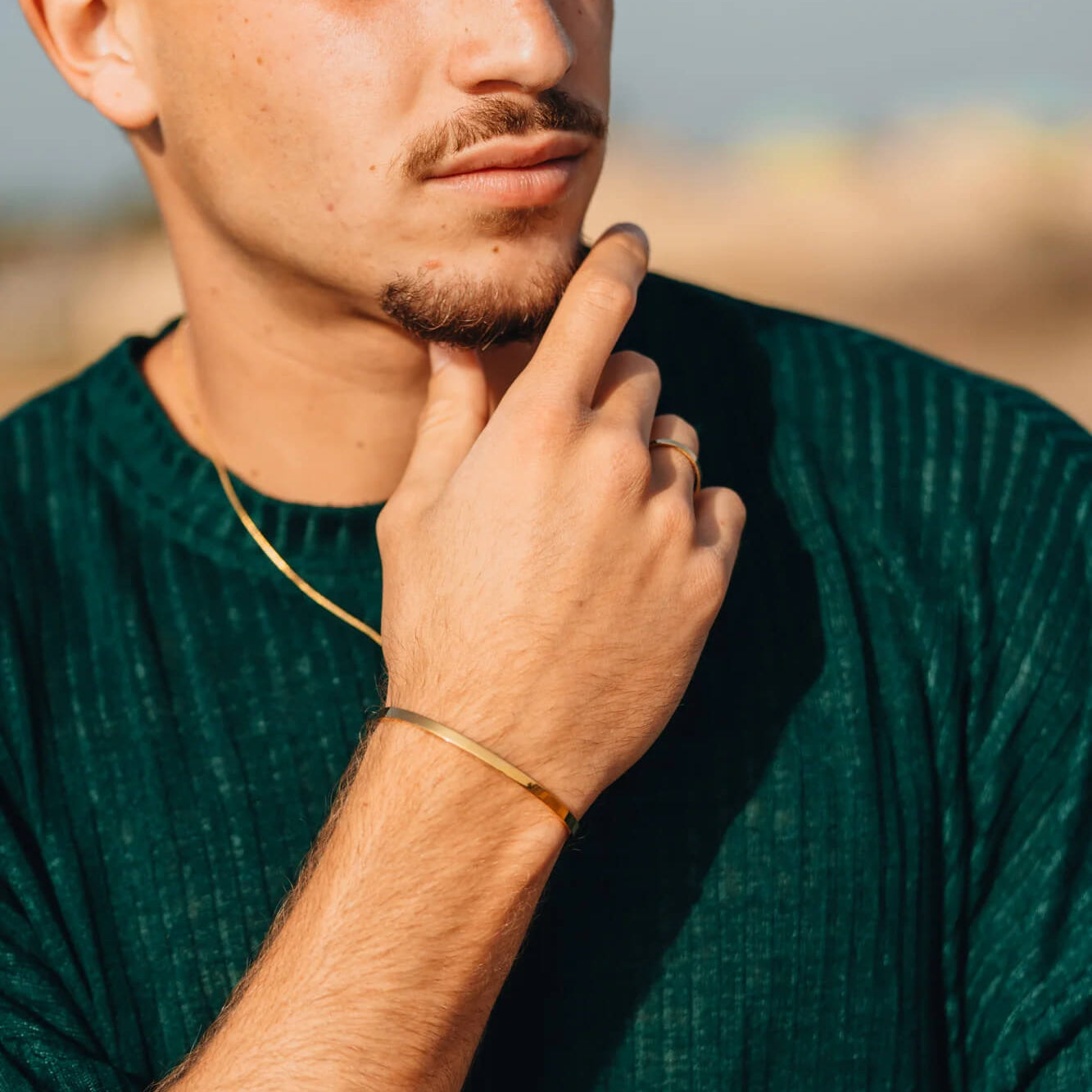 גבר בחולצה ירוקה עונד צמיד קשיח מזהב ושרשרת זהב עדינה לגבר של נרו NERO.