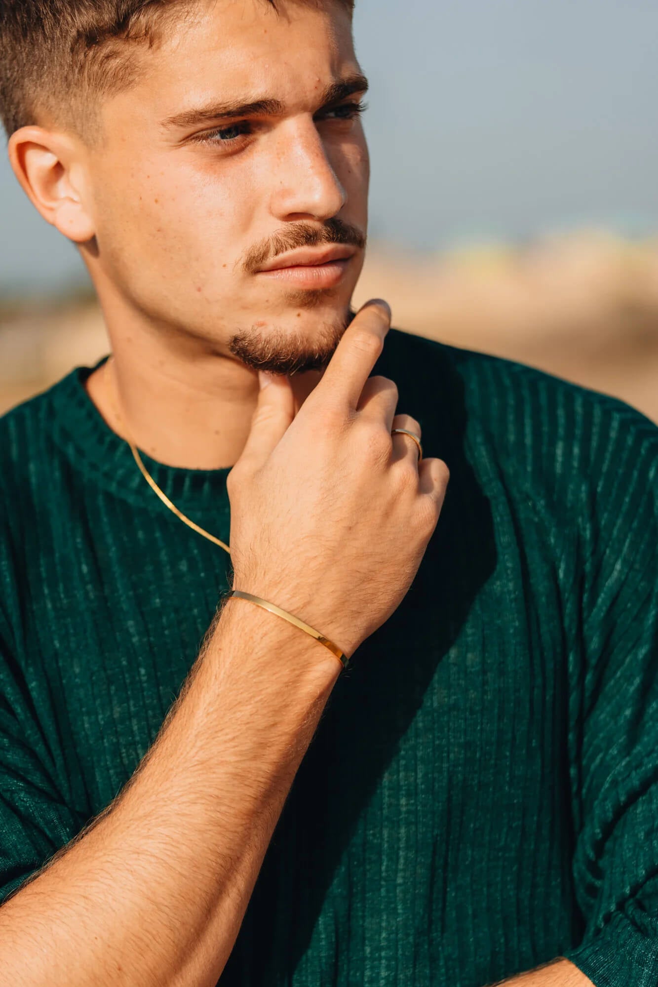 גבר בחולצה ירוקה עונד צמיד קשיח מזהב ושרשרת זהב עדינה לגבר של נרו NERO.