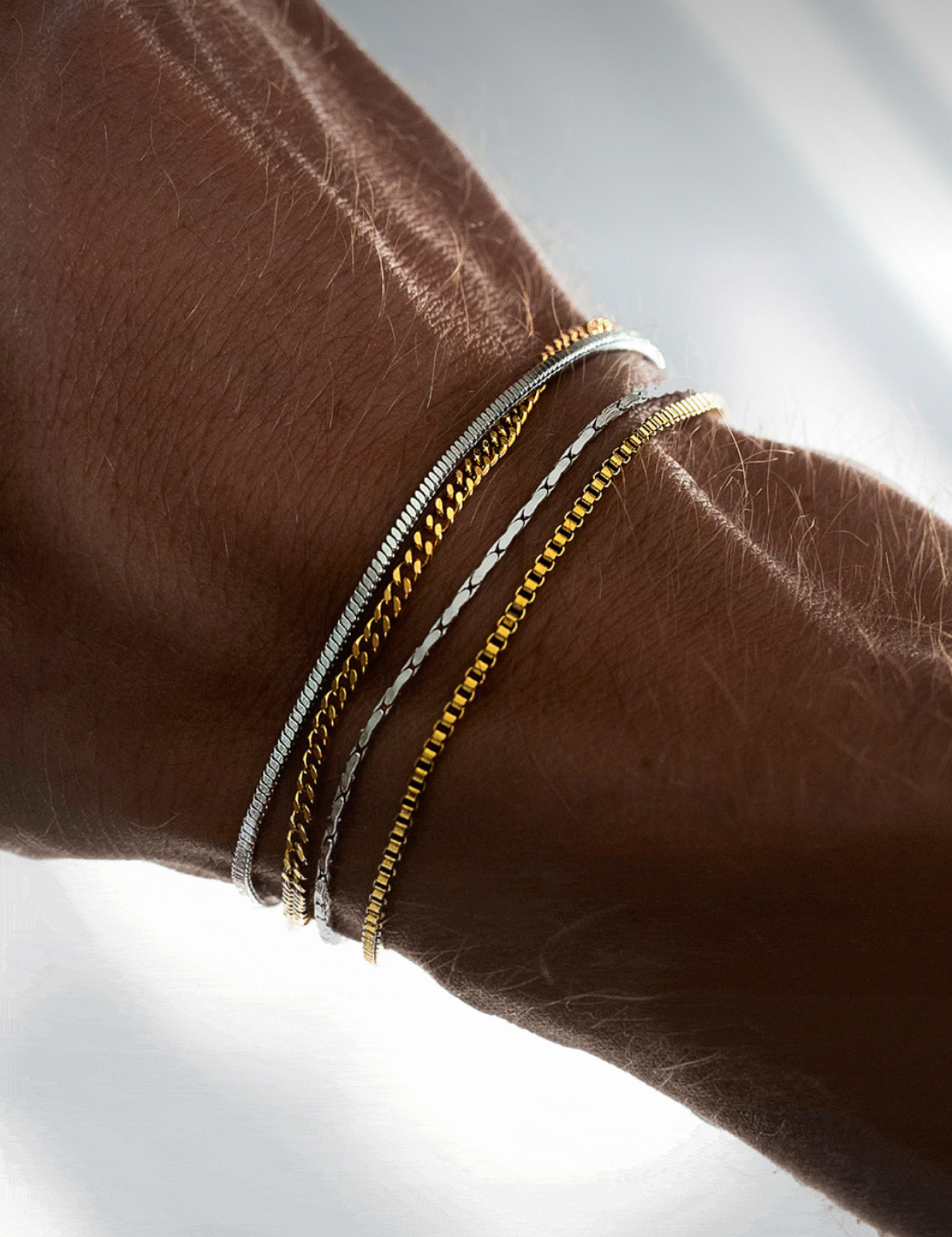 שילוב צמידי זהב וכסף לגבר מבית NERO: סט 4 צמידים דקים ומינימליסטיים בגימור מבריק הכולל שרשראות עדינות למראה שכבות מודרני.