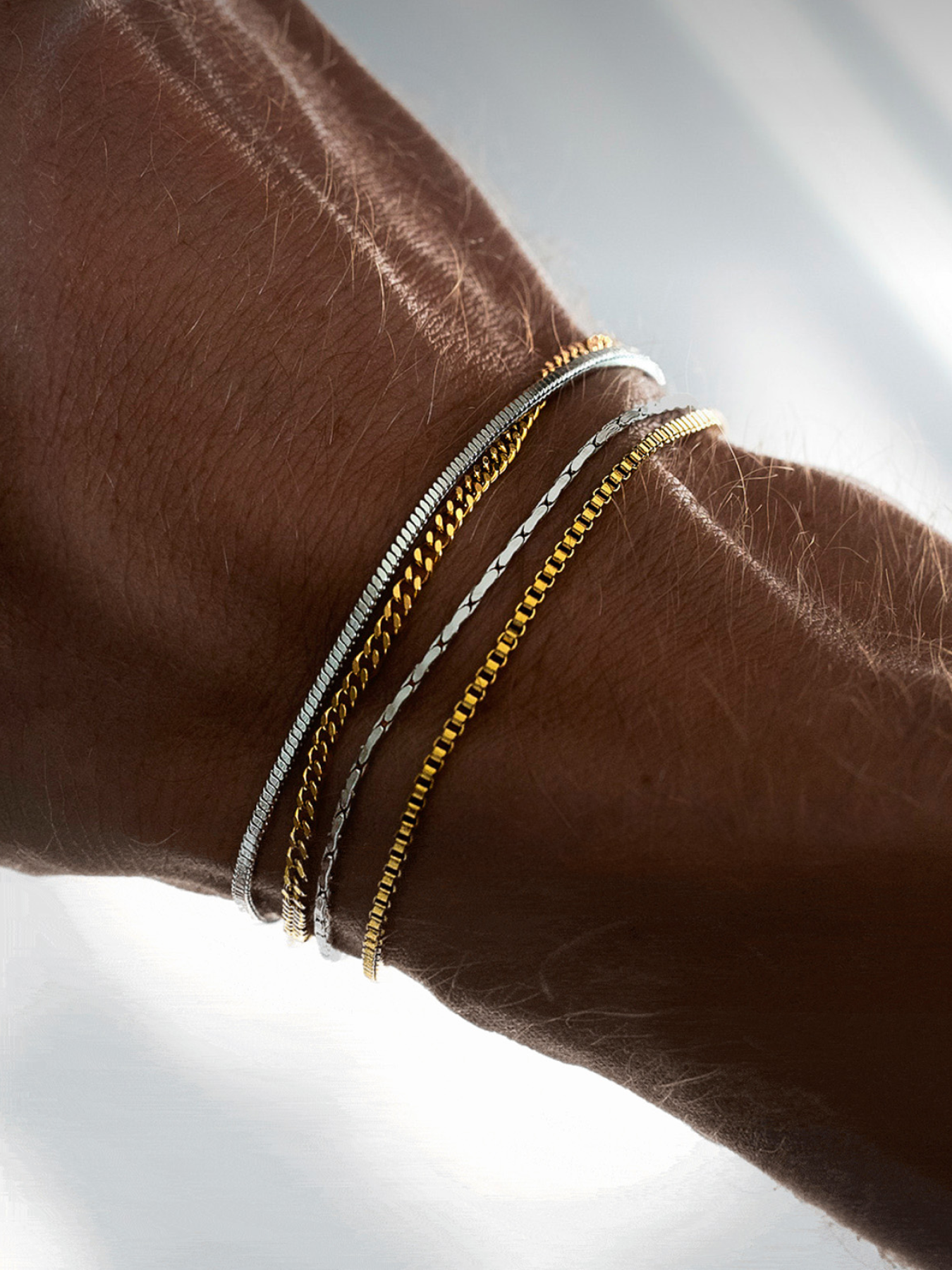 שילוב צמידי זהב וכסף לגבר מבית NERO: סט 4 צמידים דקים ומינימליסטיים בגימור מבריק הכולל שרשראות עדינות למראה שכבות מודרני.