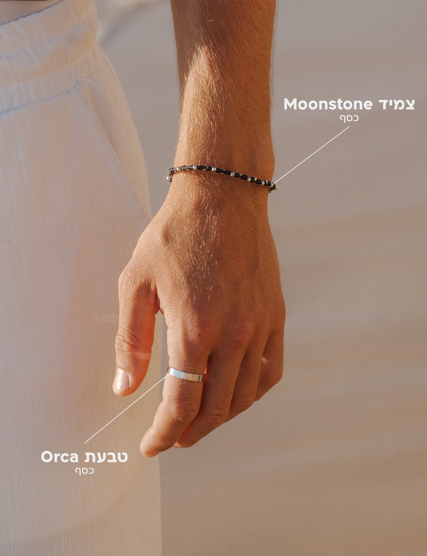 סט תכשיטי NERO לגבר: צמיד Moonstone שחור עשוי חוטי שעווה מקולקציית WILD SPIRIT משולב עם טבעת Orca מכסף בגימור מבריק על רקע לבוש לבן קיצי.