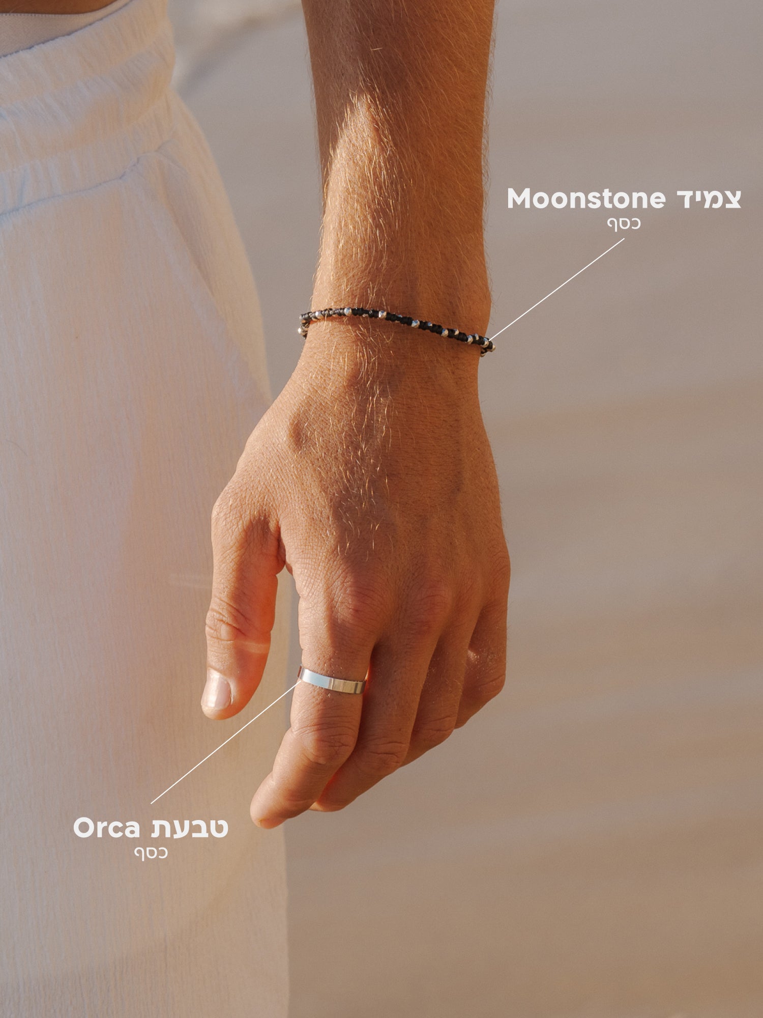 סט תכשיטי NERO לגבר: צמיד Moonstone שחור עשוי חוטי שעווה מקולקציית WILD SPIRIT משולב עם טבעת Orca מכסף בגימור מבריק על רקע לבוש לבן קיצי.