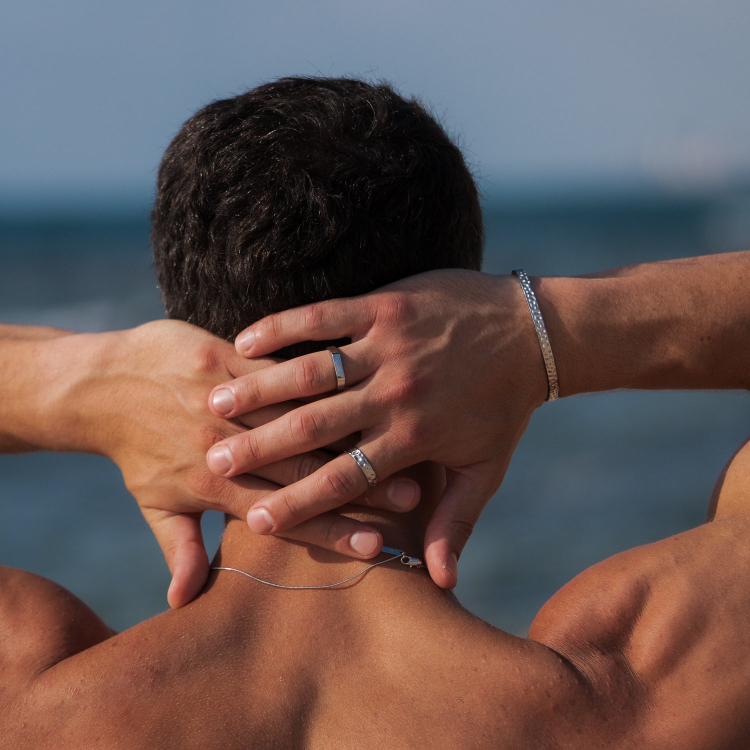 גבר עונד צמיד כסף וטבעות של מותג התכשיטים נרו (Nero) על רקע הים, משדר ביטחון עצמי ונוכחות שקטה.