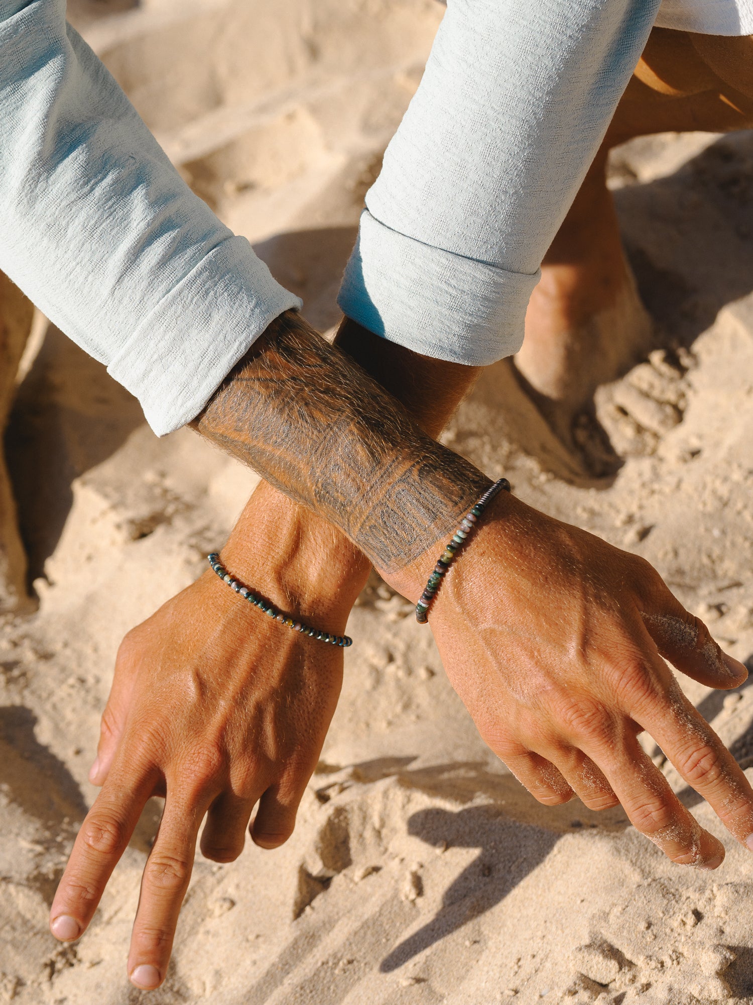 סט של צמיד Onyx שחור מבריק (אגט) עם צמיד Reef כסף וטבעת Polar, על חול רטוב.