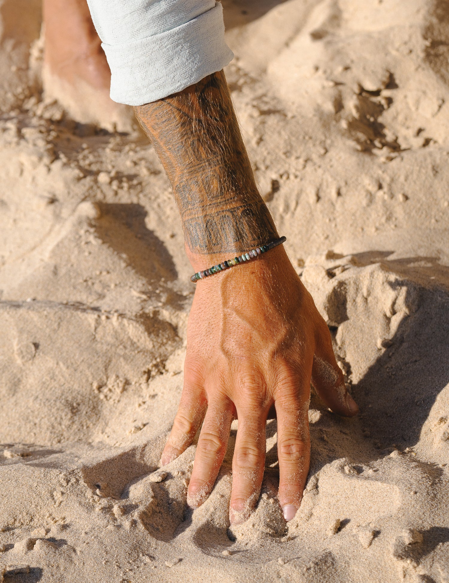 סט תכשיטים: צמיד Onyx שחור, צמיד Reef כסף, מונחים על חול יבש.