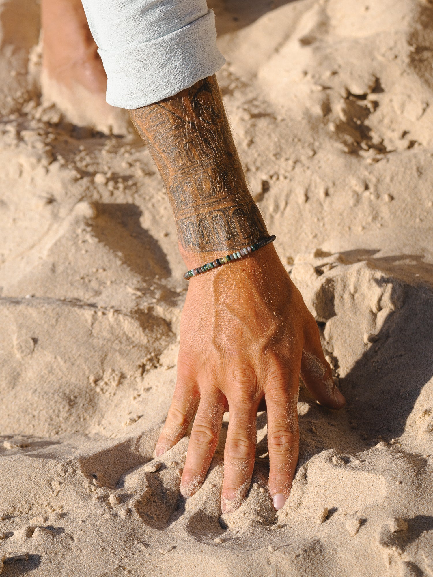 סט תכשיטים: צמיד Onyx שחור, צמיד Reef כסף, מונחים על חול יבש.