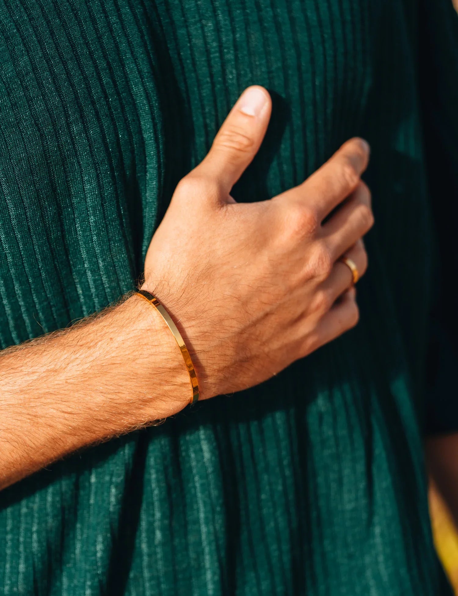 צמיד Orca מוזהב על פרק יד של גבר, מצולם בתאורה טבעית עם חולצה ירוקה טקסטורלית