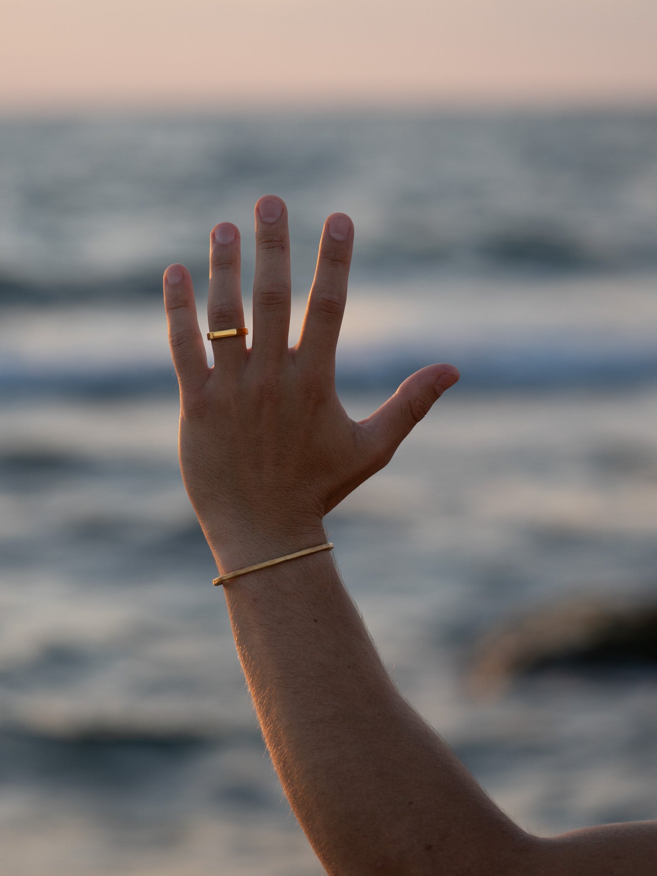 טבעת Polar זהב מבריקה על יד גברית מורמת מול רקע הים בשעת שקיעה.
