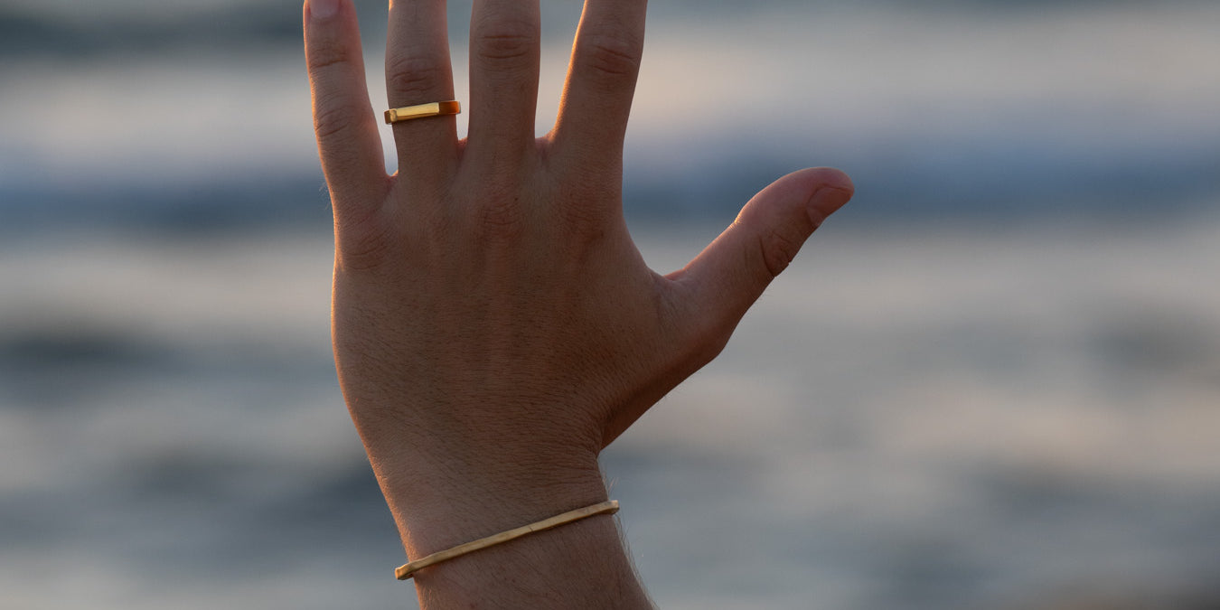 טבעת Polar זהב מבריקה על יד גברית מורמת מול רקע הים בשעת שקיעה.