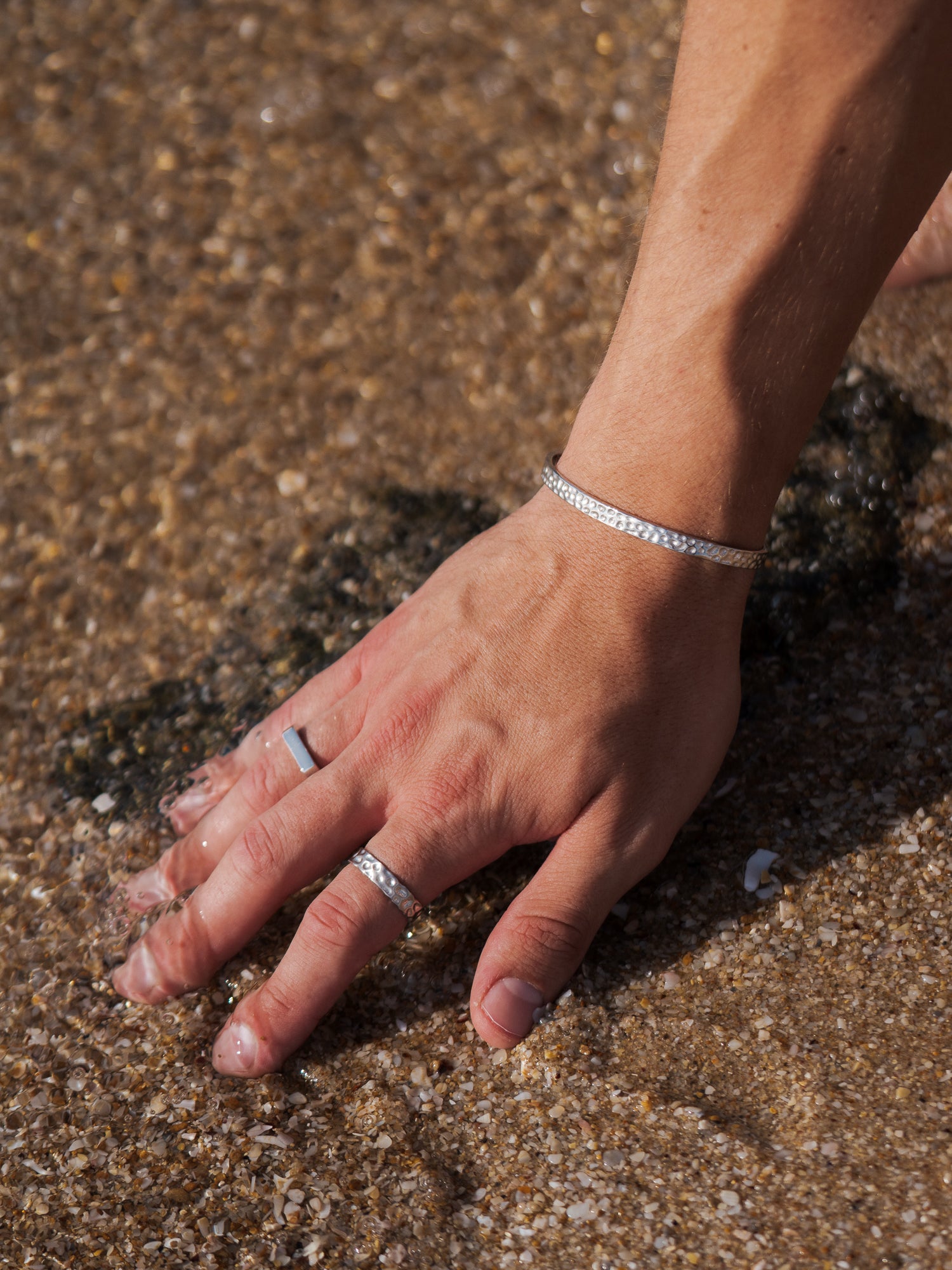 טבעת Polar כסף מבריקה על יד גברית, מונחת על חול רטוב ומים רדודים.