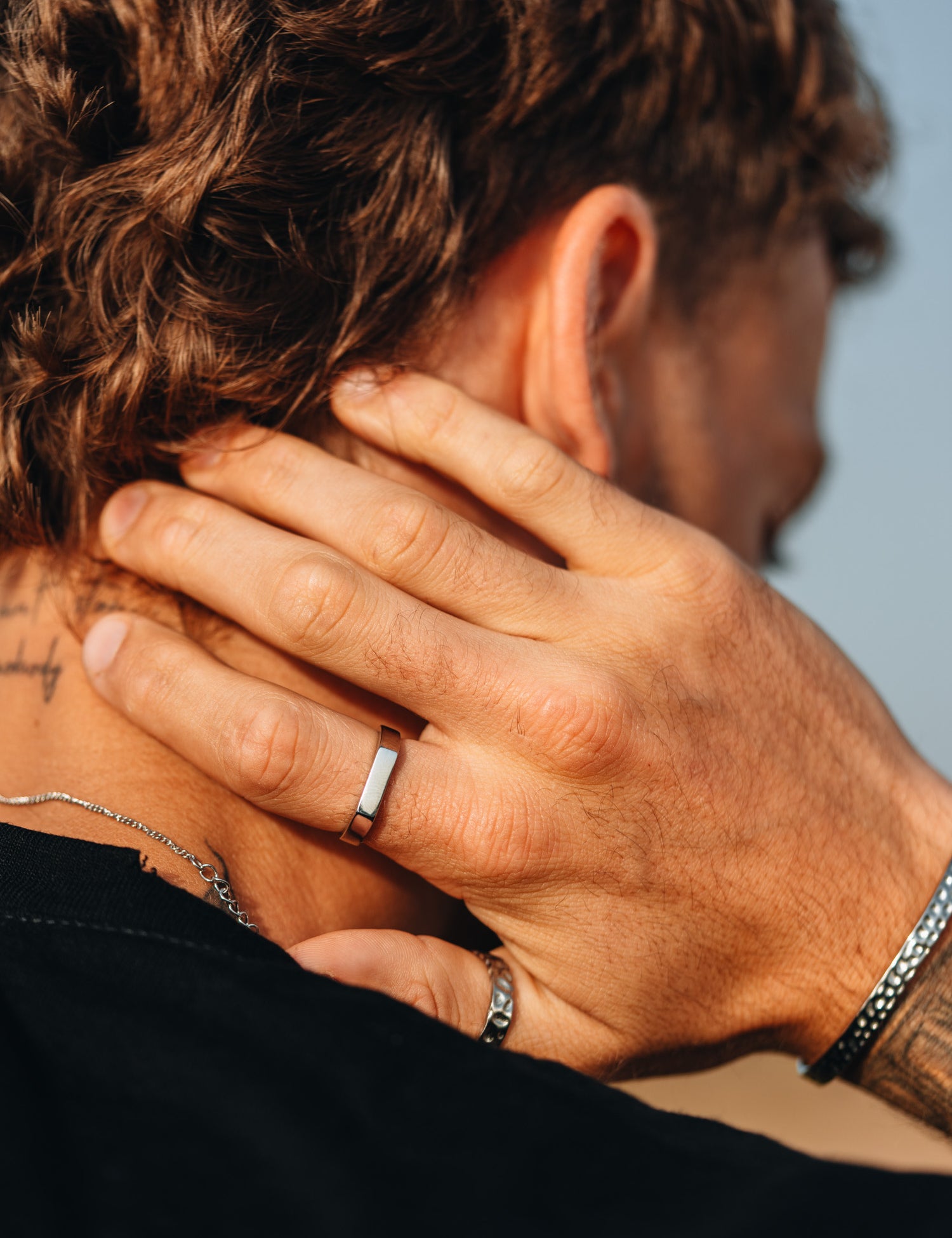 טבעת Polar כסף מבריקה על אצבע גברית, בצילום תקריב עם צמיד וקעקוע.