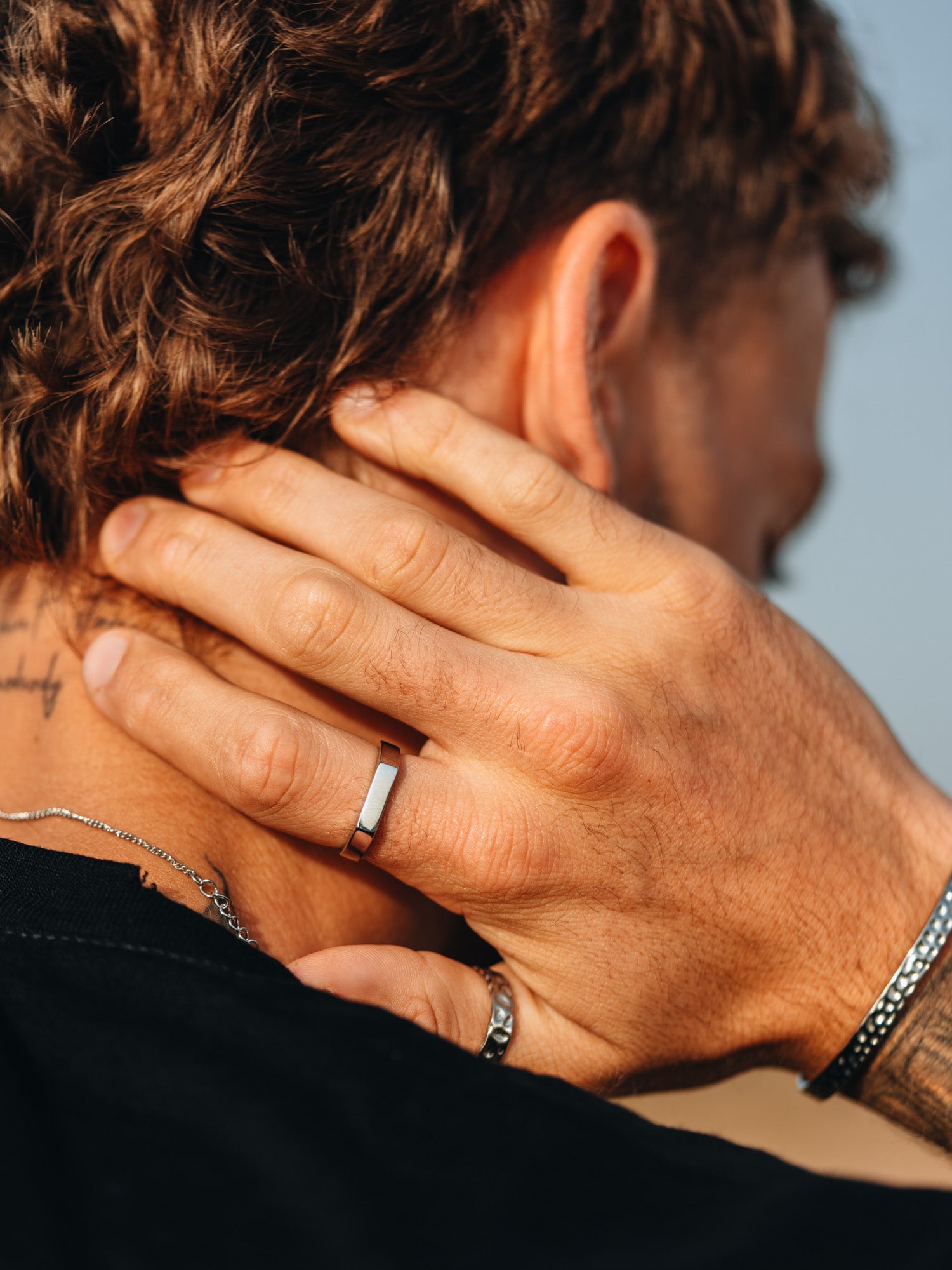 טבעת Polar כסף מבריקה על אצבע גברית, בצילום תקריב עם צמיד וקעקוע.