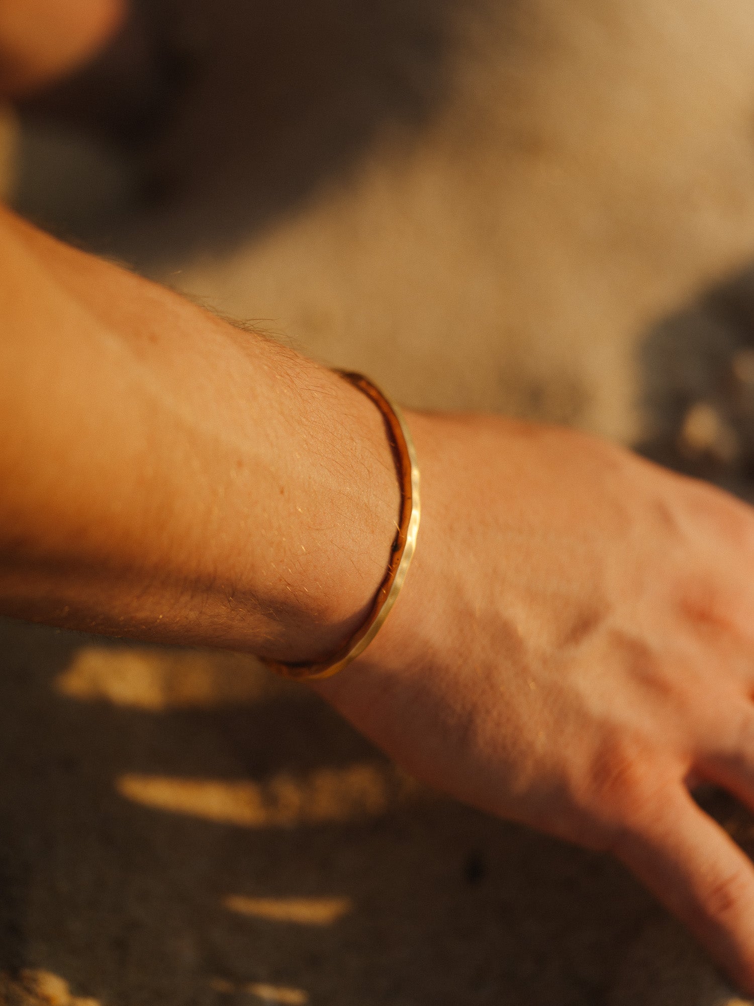 צמיד Reef זהב מט על יד גברית, בצילום תקריב על רקע חול.