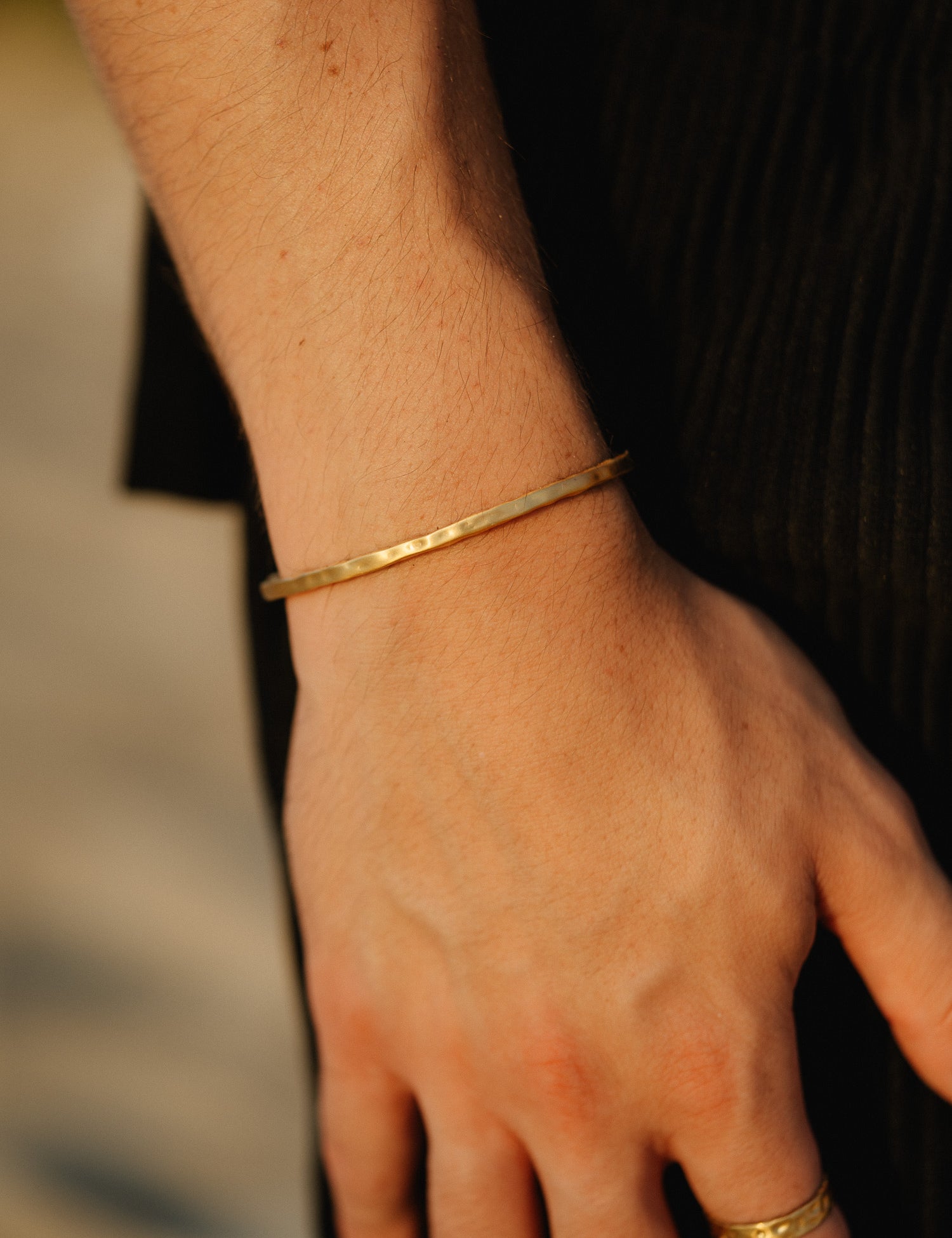 צמיד Reef זהב מט על יד גברית, משולב בטבעת זהב, עם חולצה שחורה.