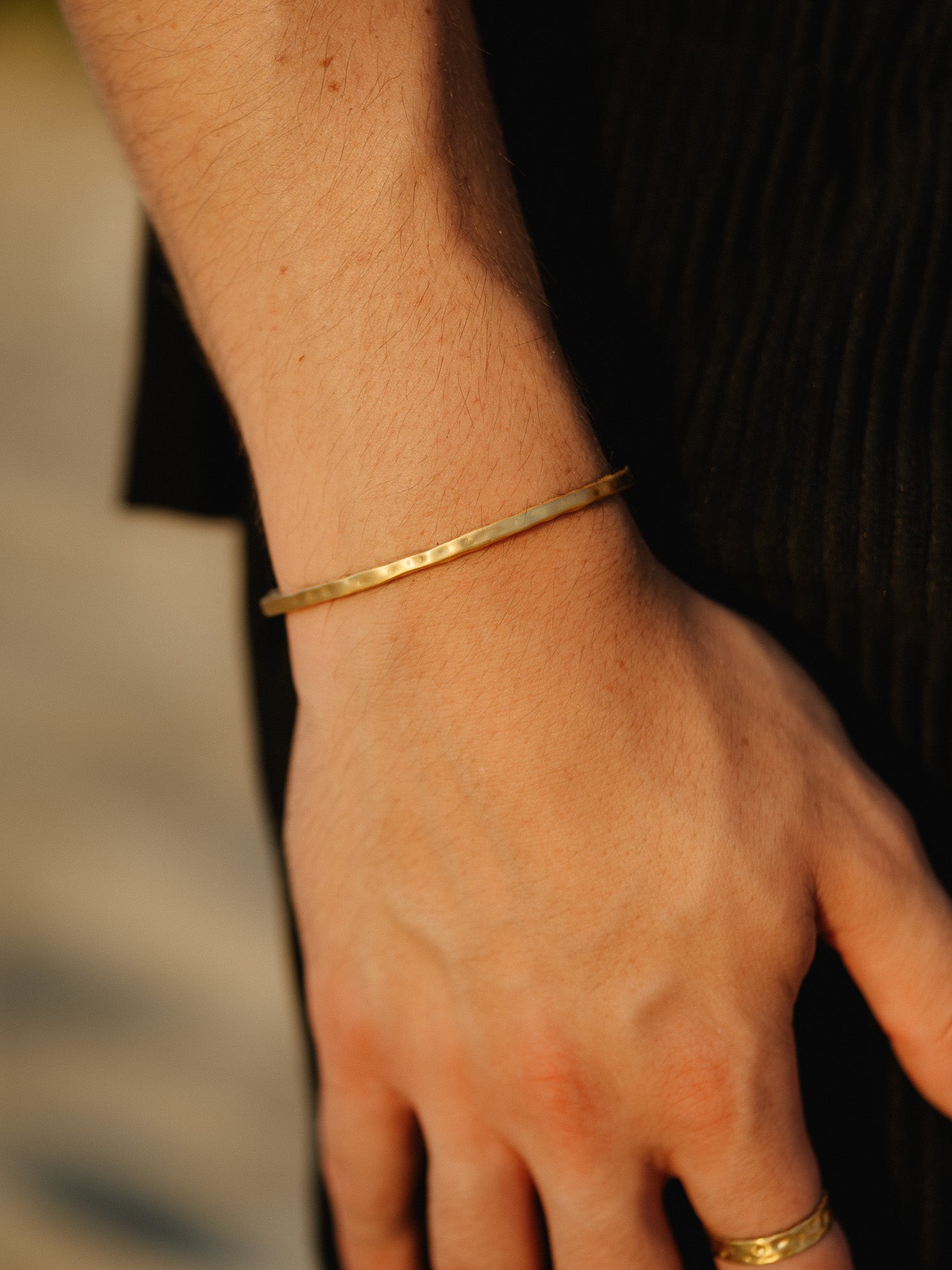 צמיד Reef זהב מט על יד גברית, משולב בטבעת זהב, עם חולצה שחורה.