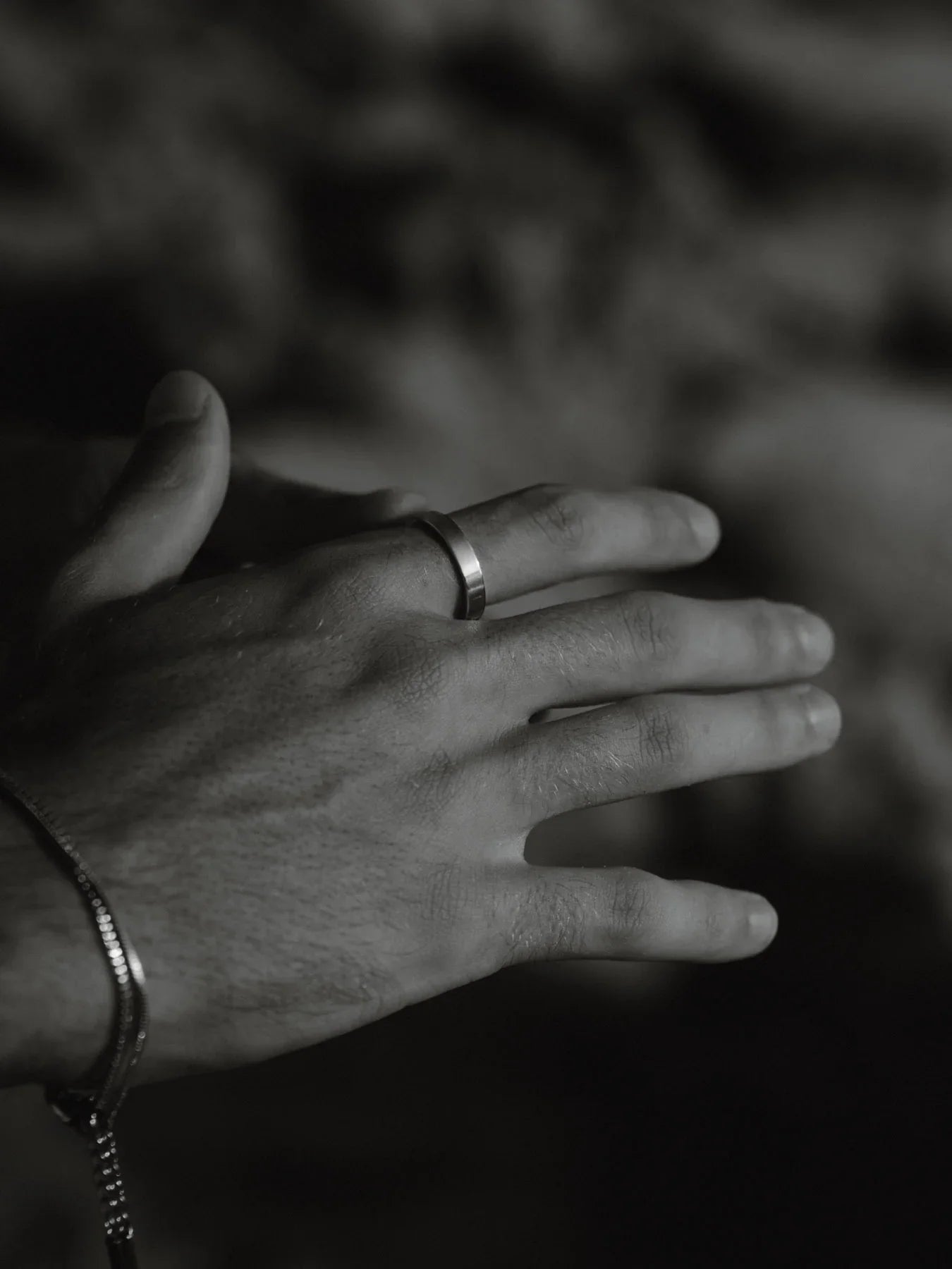 צילום שחור־לבן של יד גבר העונדת טבעת כסף מינימליסטית וצמיד דק, על רקע מטושטש.