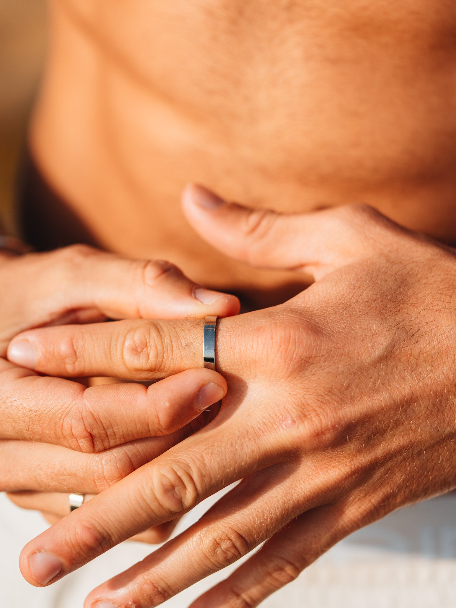 גבר עונד טבעת כסף דקה בסגנון מינימליסטי על רקע חוף, צילום תקריב של כף היד והאצבעות.