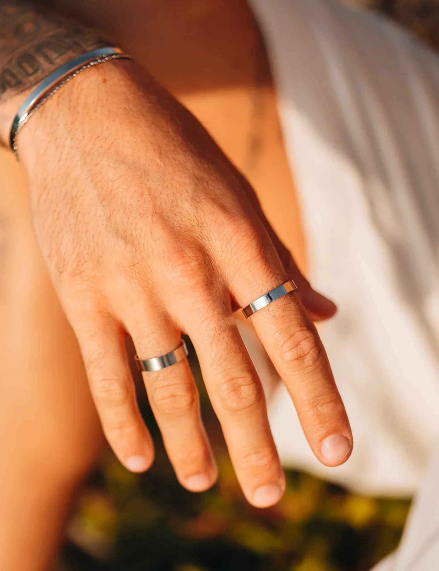 יד של גבר עם שתי טבעות כסף מינימליסטיות על האצבעות ברקע חוף וטבע